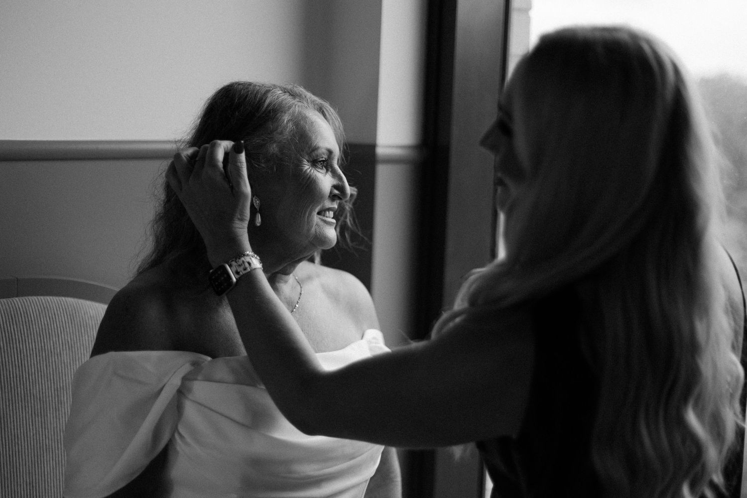 Woman helping a bride adjust her hair near a window before the wedding ceremony.