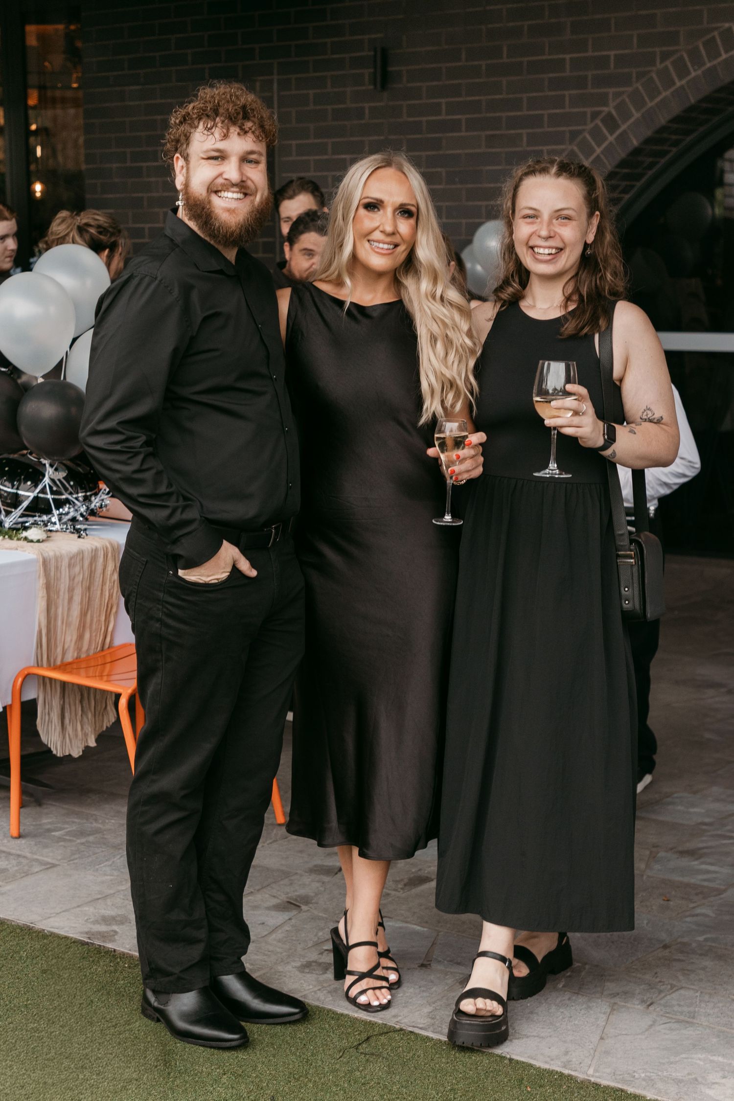 Three friends in black outfits smiling together at an elegant evening celebration.