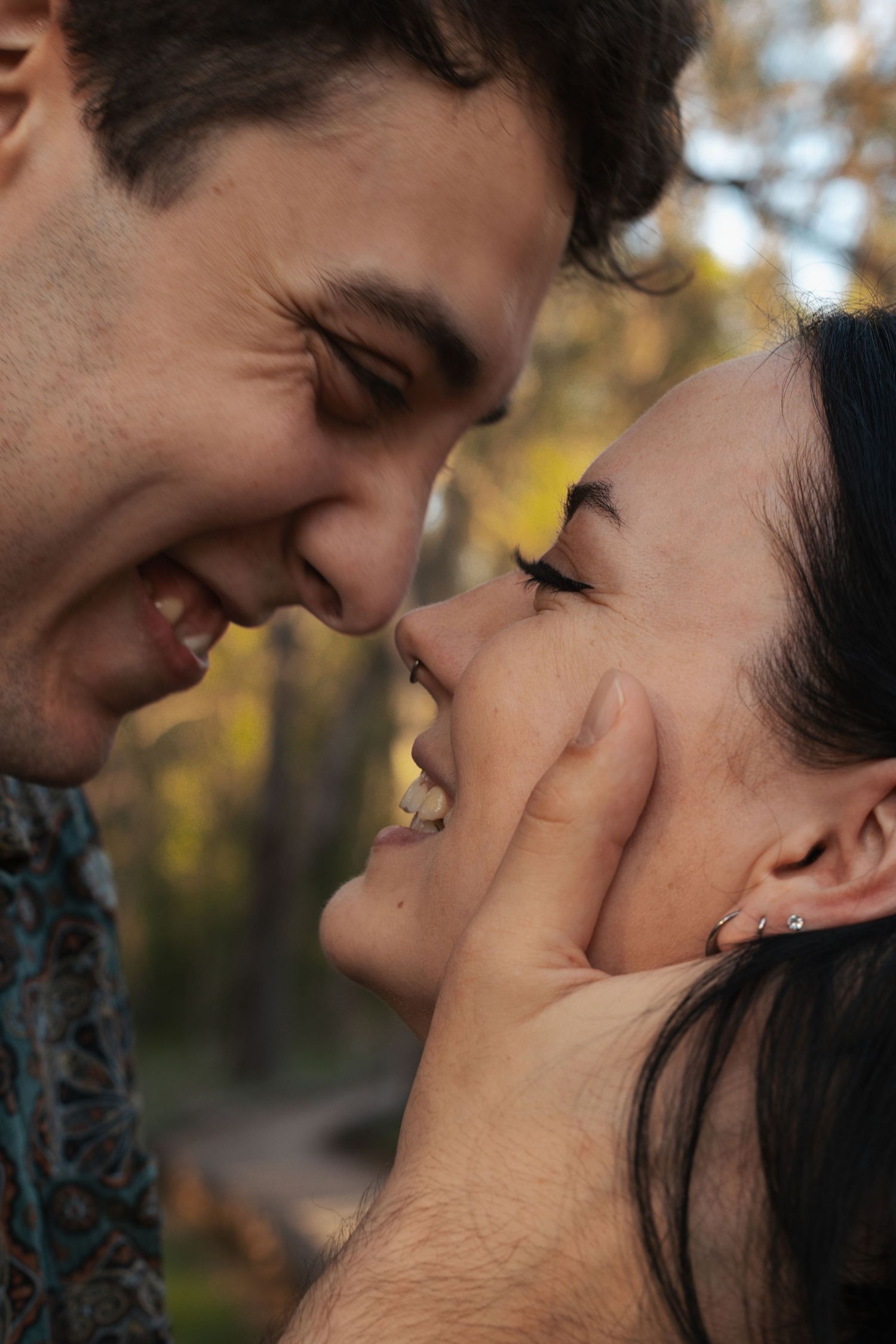Close-up of smiling couple nearly kissing, man tenderly holding womans face in warm outdoor light.