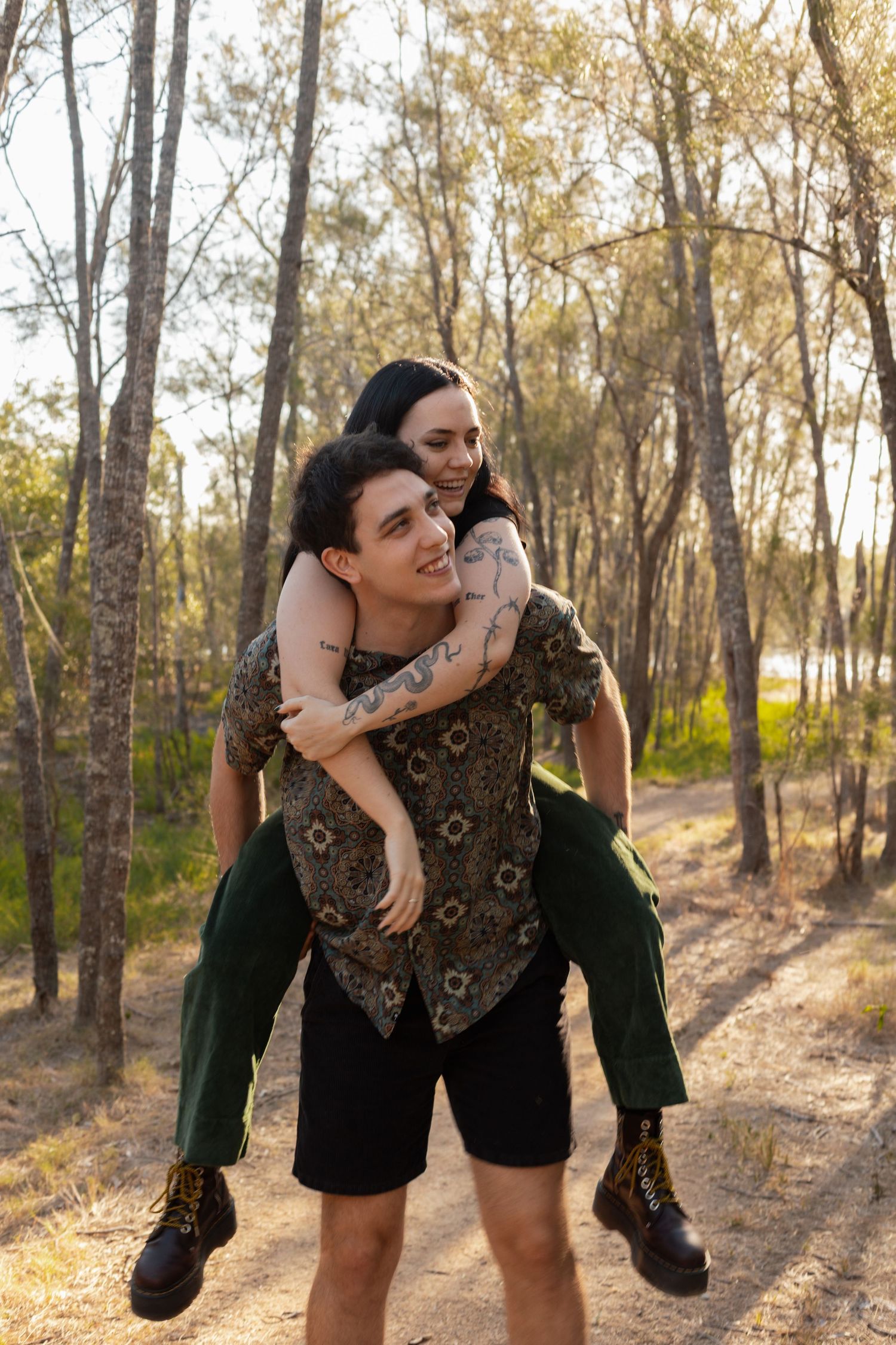 Man giving smiling woman a piggyback ride on a sunny forest trail, both laughing and enjoying the moment.