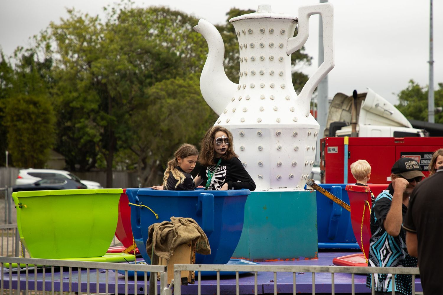 Two children in Halloween costumes ride teacup carnival attraction at outdoor Halloween festival.