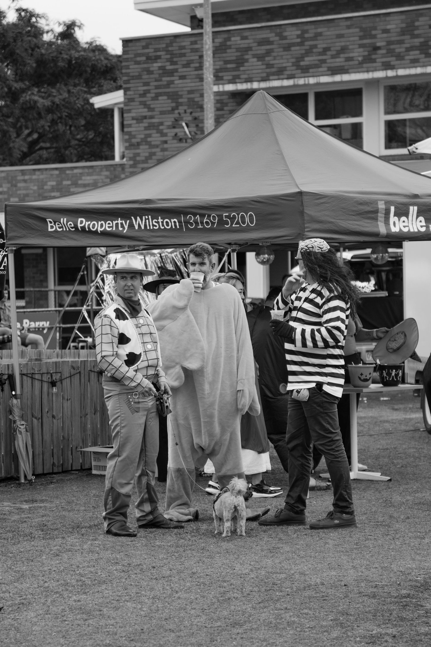 Black and white photo of three costumed adults with a small dog at a Belle Property Wilston Halloween event.