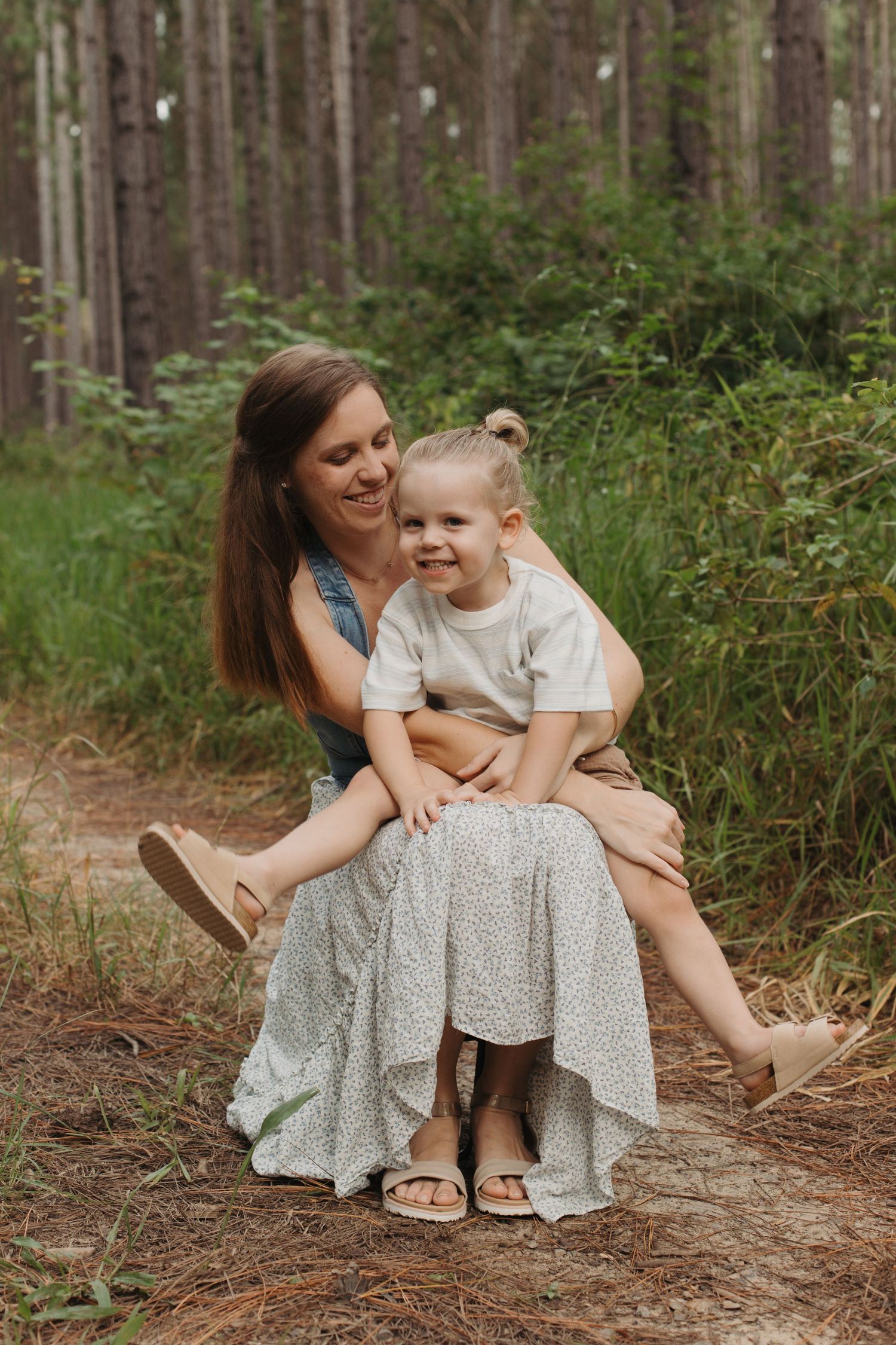 Mother sitting with toddler on a forest path during a family photo shoot.