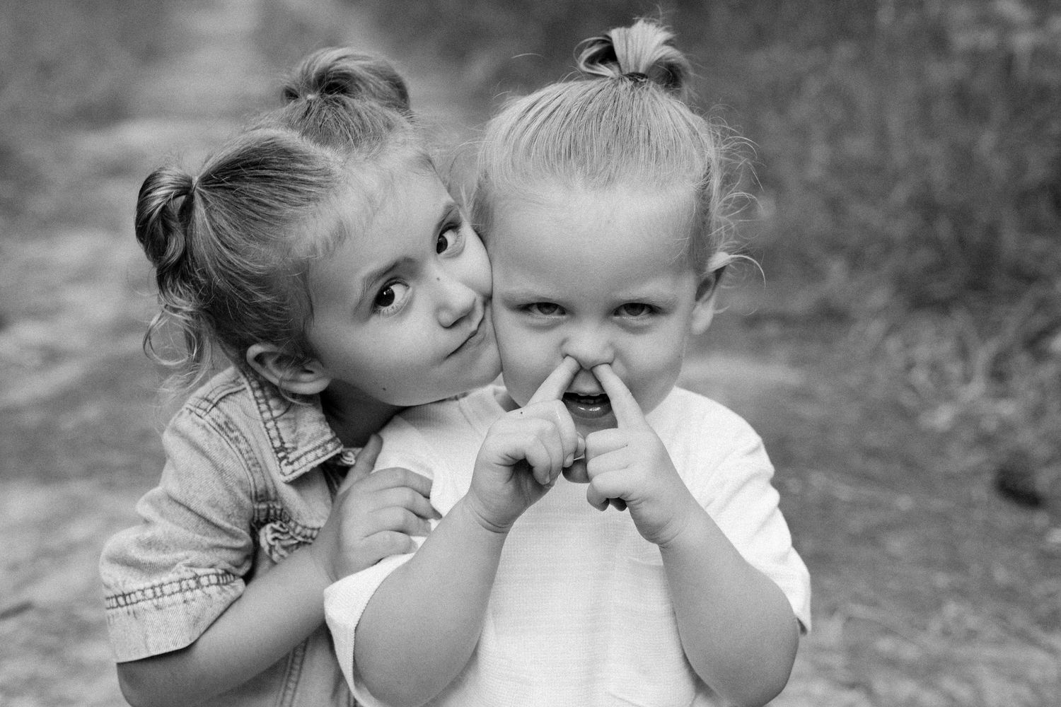 Two young children pose together playfully in a black and white portrait photo.