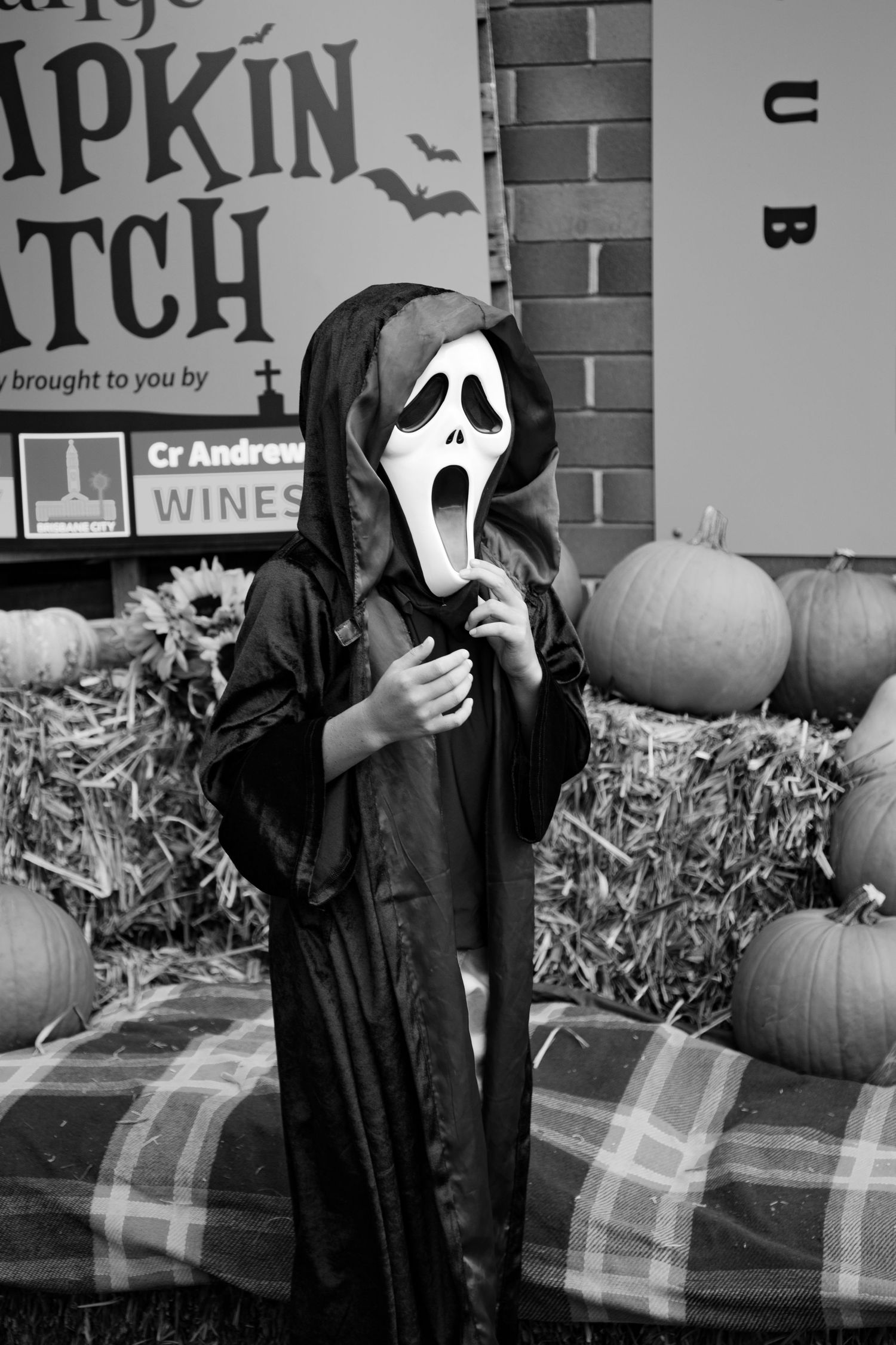 Child dressed in Ghostface Scream Halloween costume posing at Grange Pumpkin Patch in black and white.