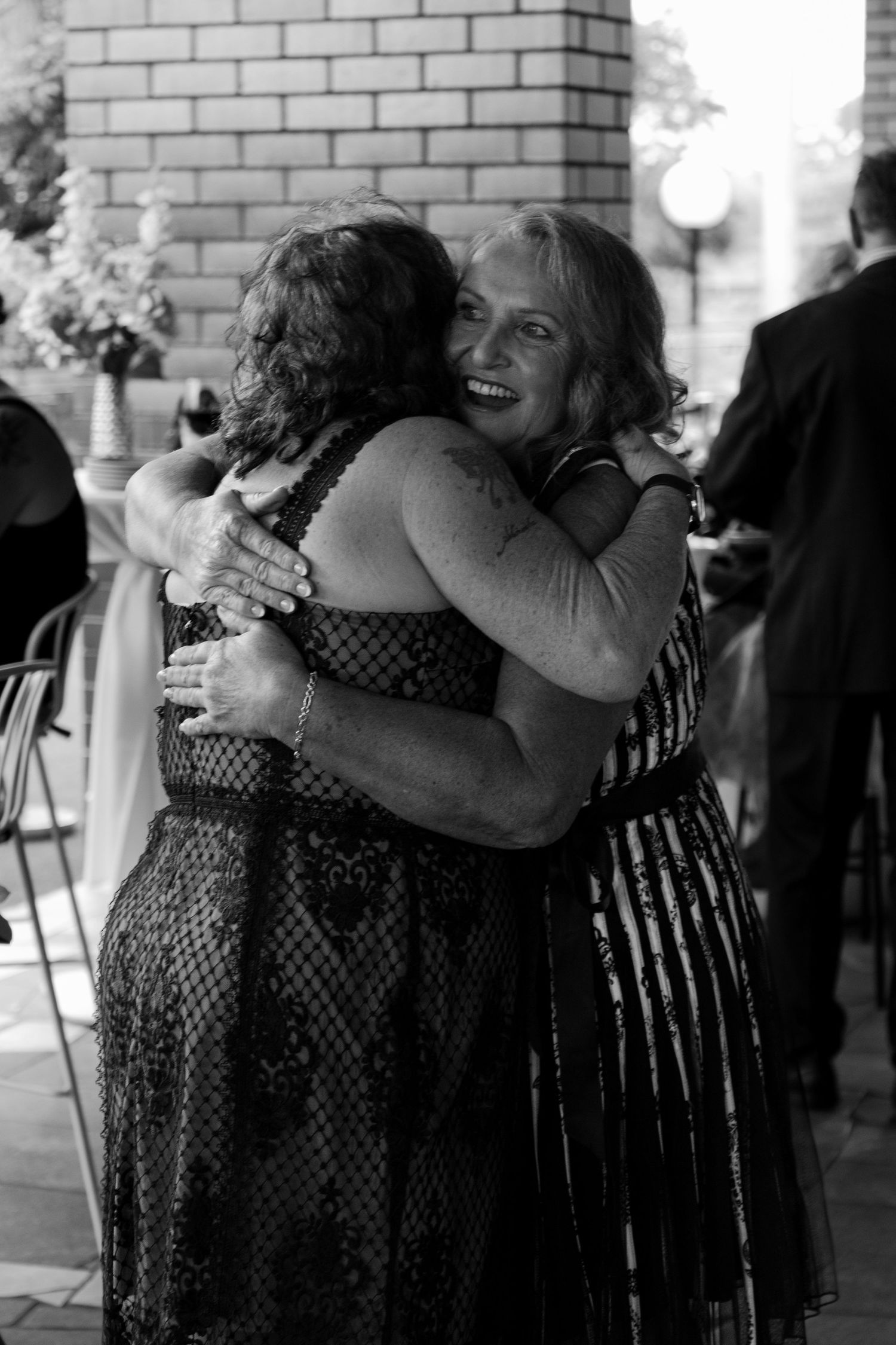 Two women sharing a warm embrace and smiling at an outdoor wedding reception.