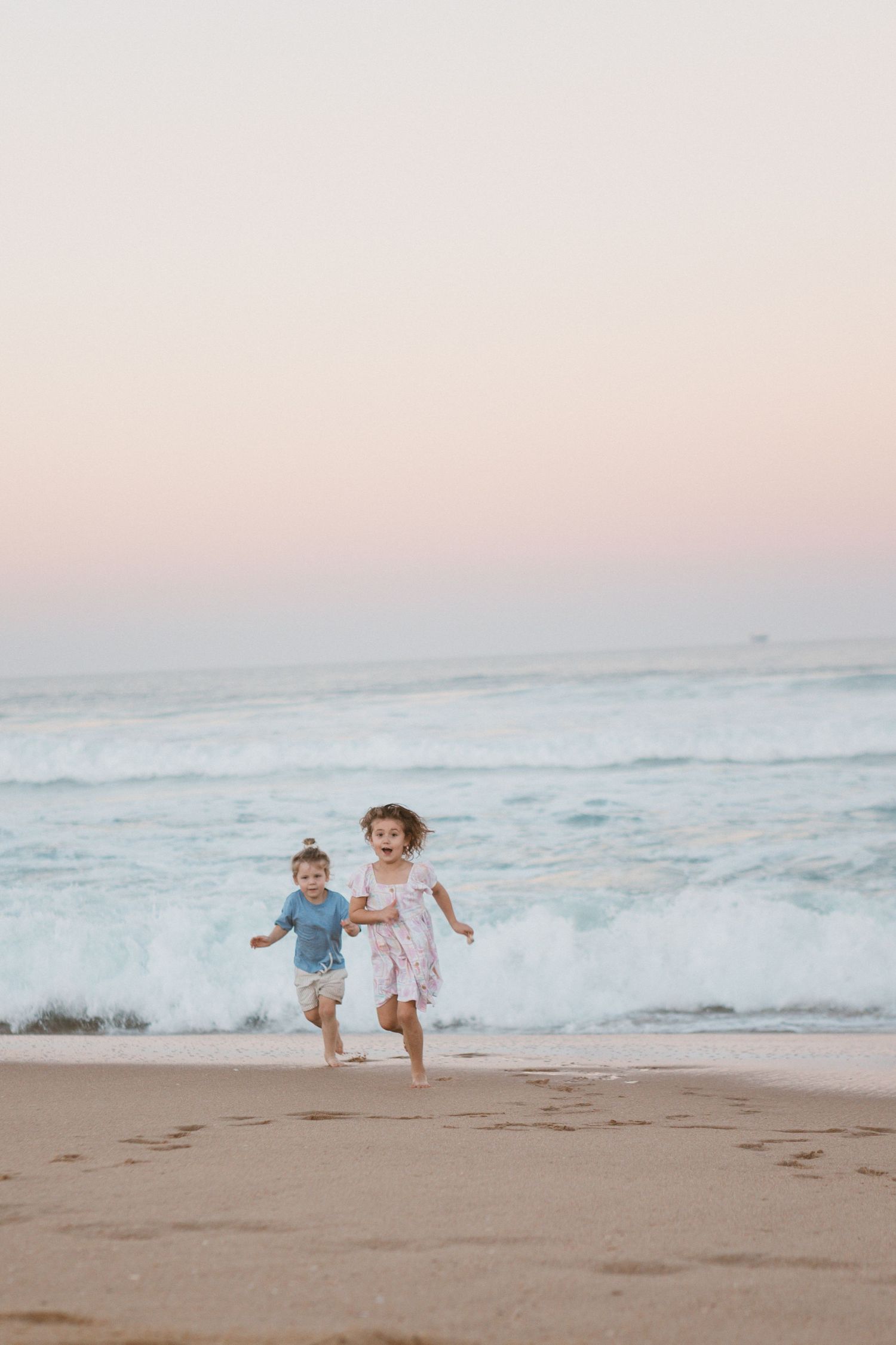 Two children running along the beach during a sunset family photo session.