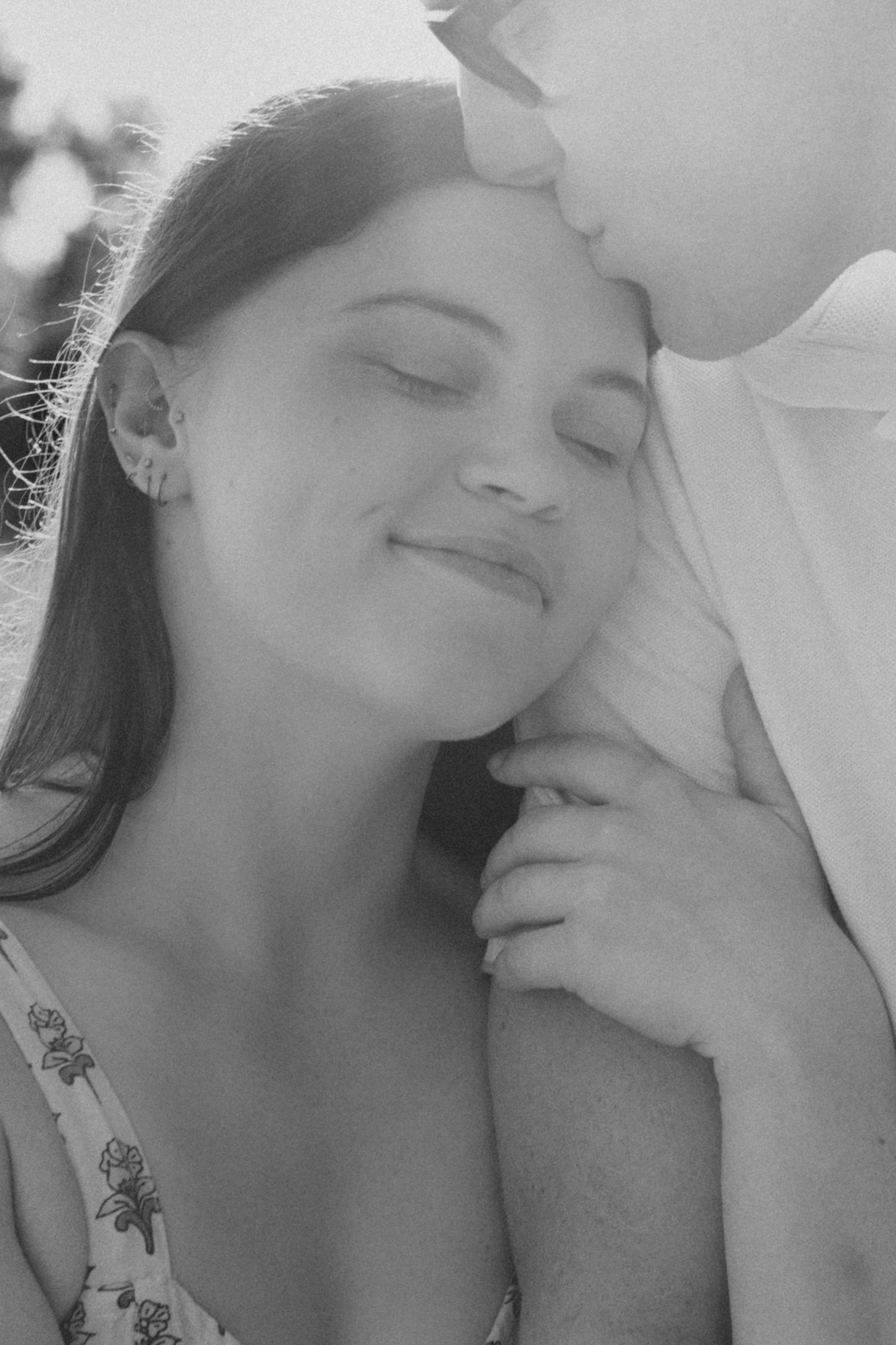 Black and white close-up of woman smiling peacefully as partner kisses her cheek tenderly.