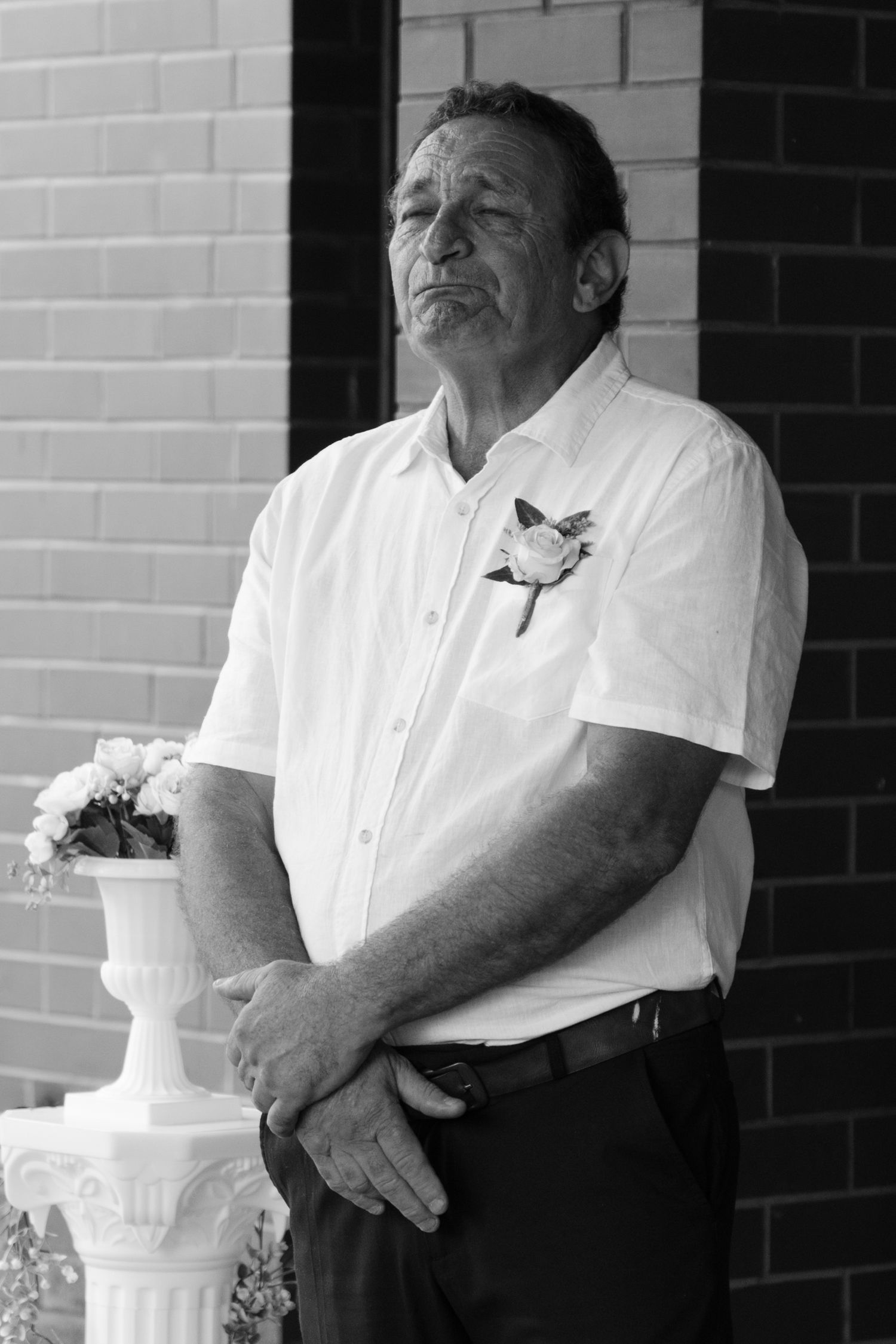 Emotional groom in white shirt with boutonniere looking up thoughtfully before wedding ceremony in black and white.