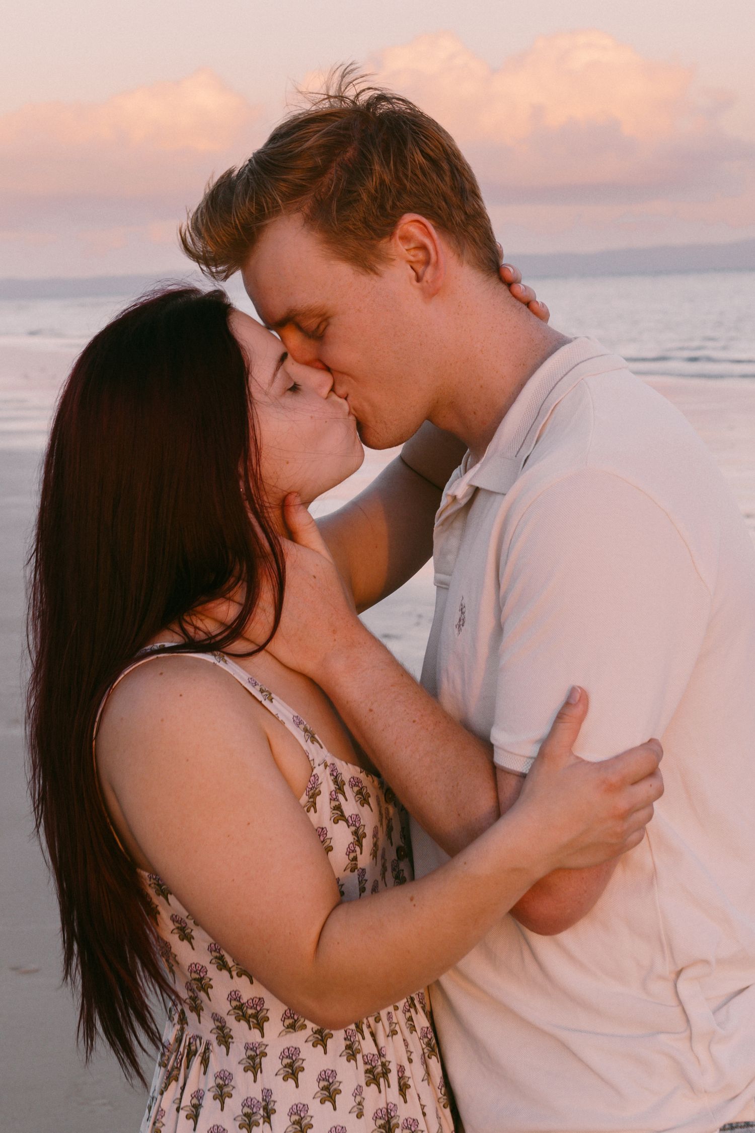 Romantic couple sharing a kiss on the beach at sunset with ocean waves in the background.