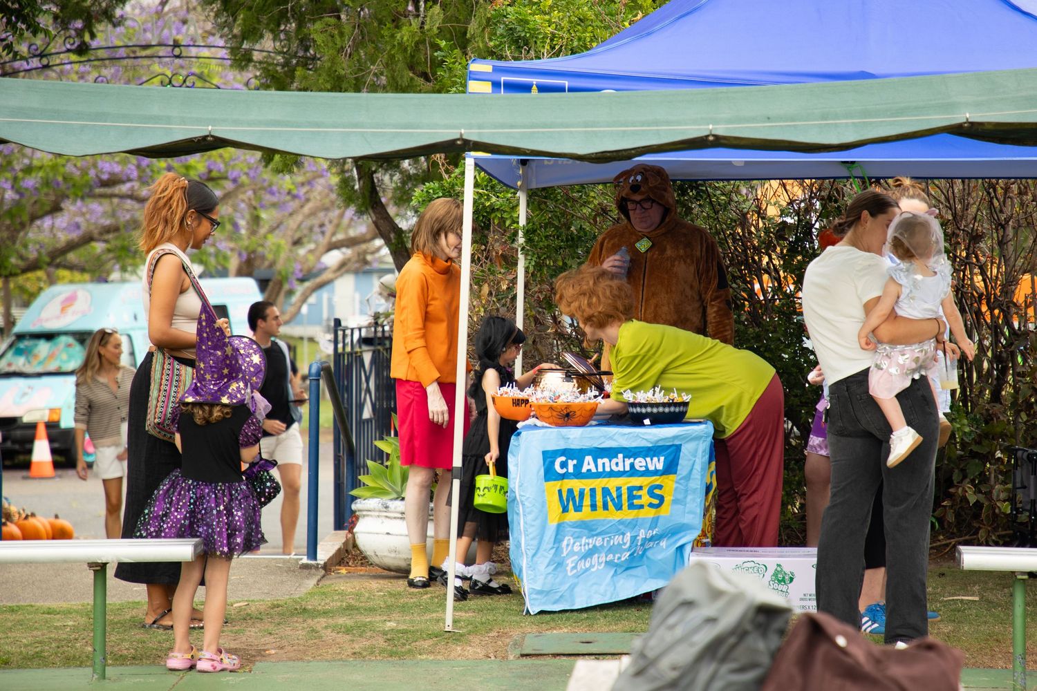 Families browse a Halloween event booth sponsored by Cr Andrew Wines at an outdoor community fair.