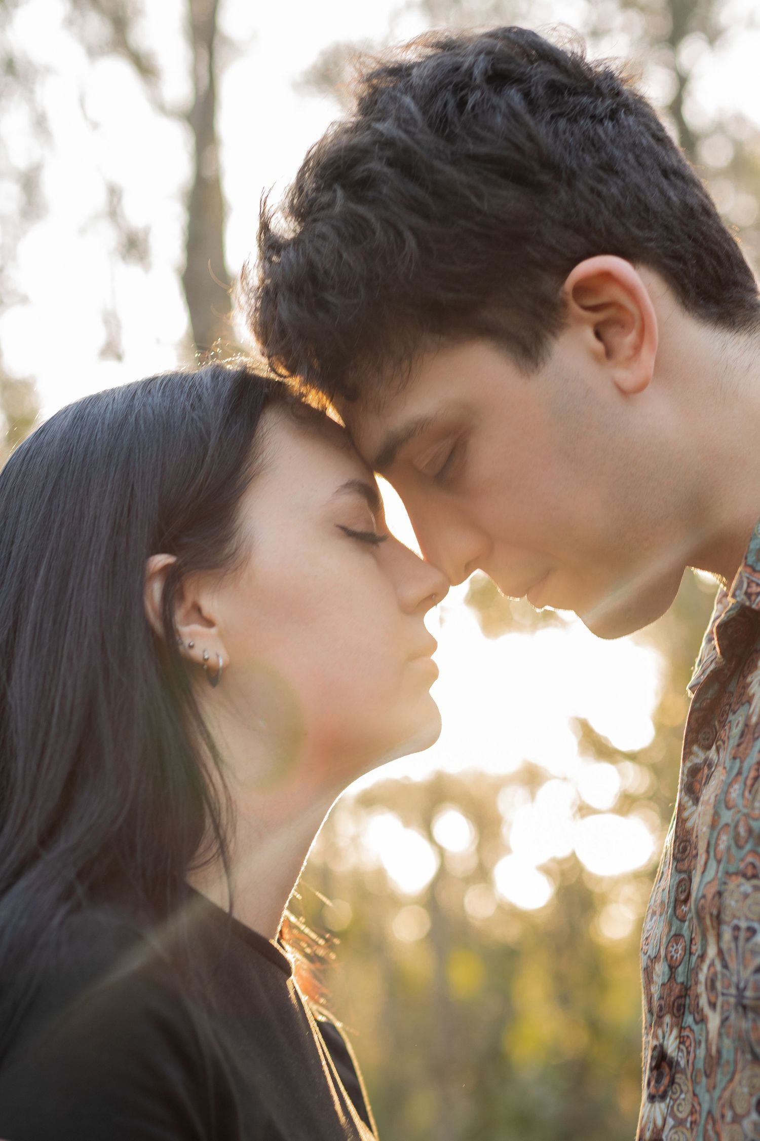 Close-up profile of a young couple with eyes closed, foreheads touching in golden light.