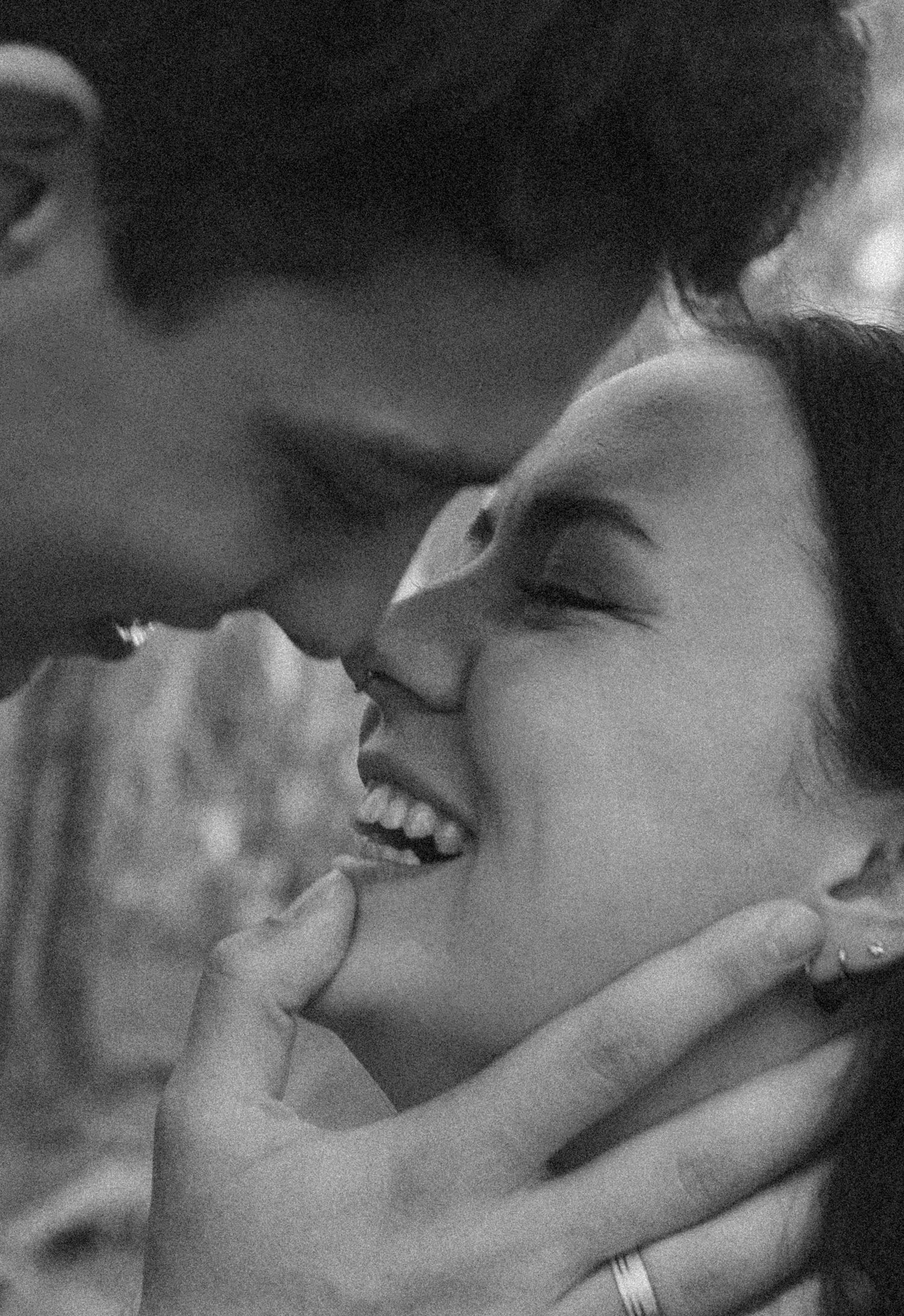 Black and white photo of a couple almost kissing, man gently holding woman's face as she smiles with eyes closed.