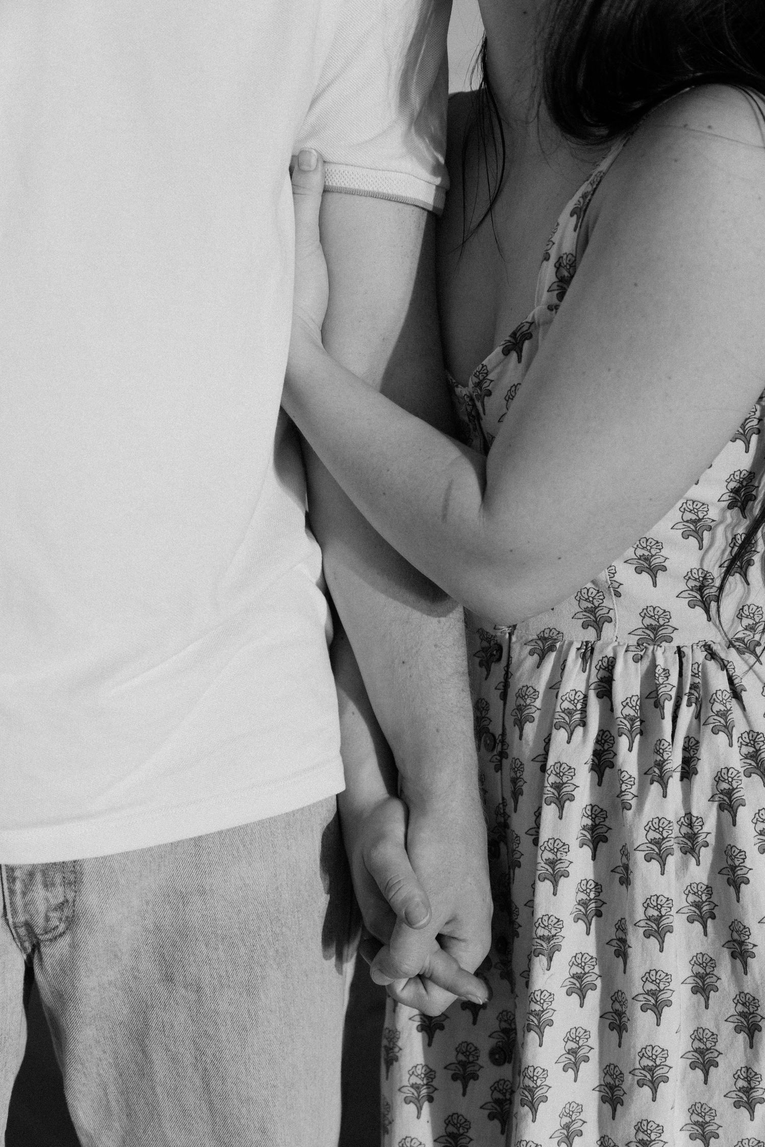 Black and white photo of a couple holding hands and embracing, woman in floral dress.