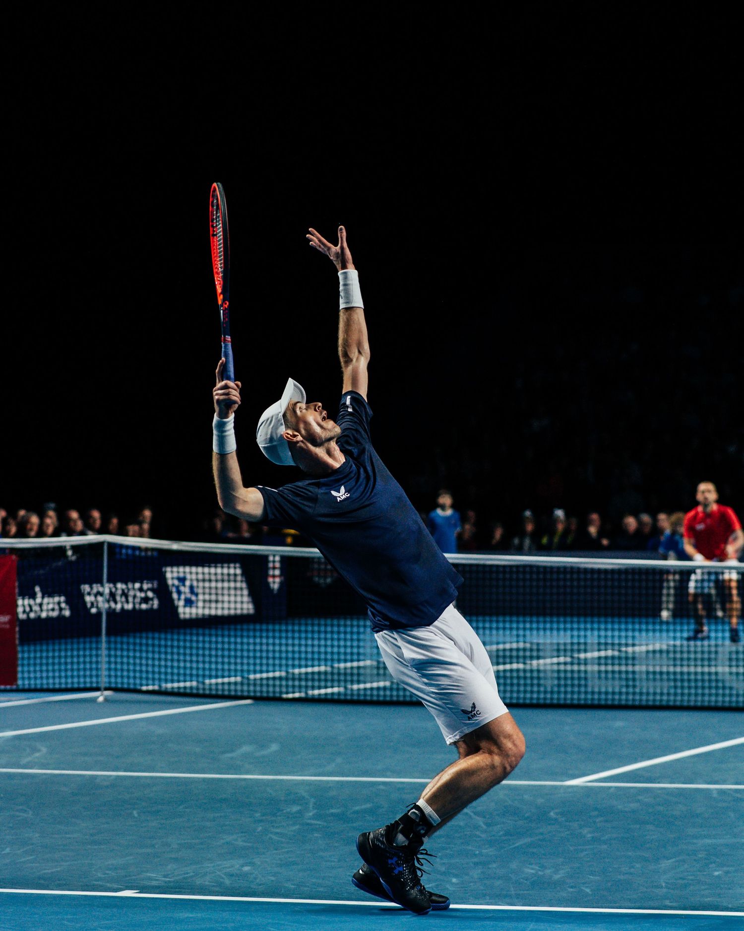 Tennis player in navy Castore kit serving on blue court at Battle of the Brits event.