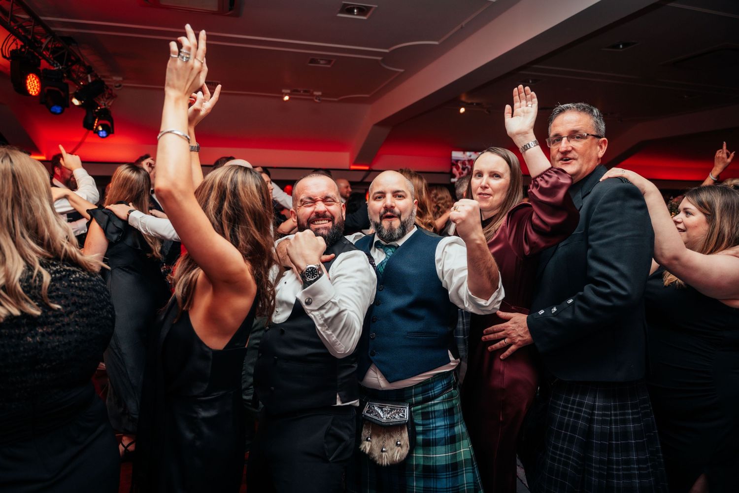 Guests in kilts and formal wear dancing energetically at a lively Burns Night celebration.
