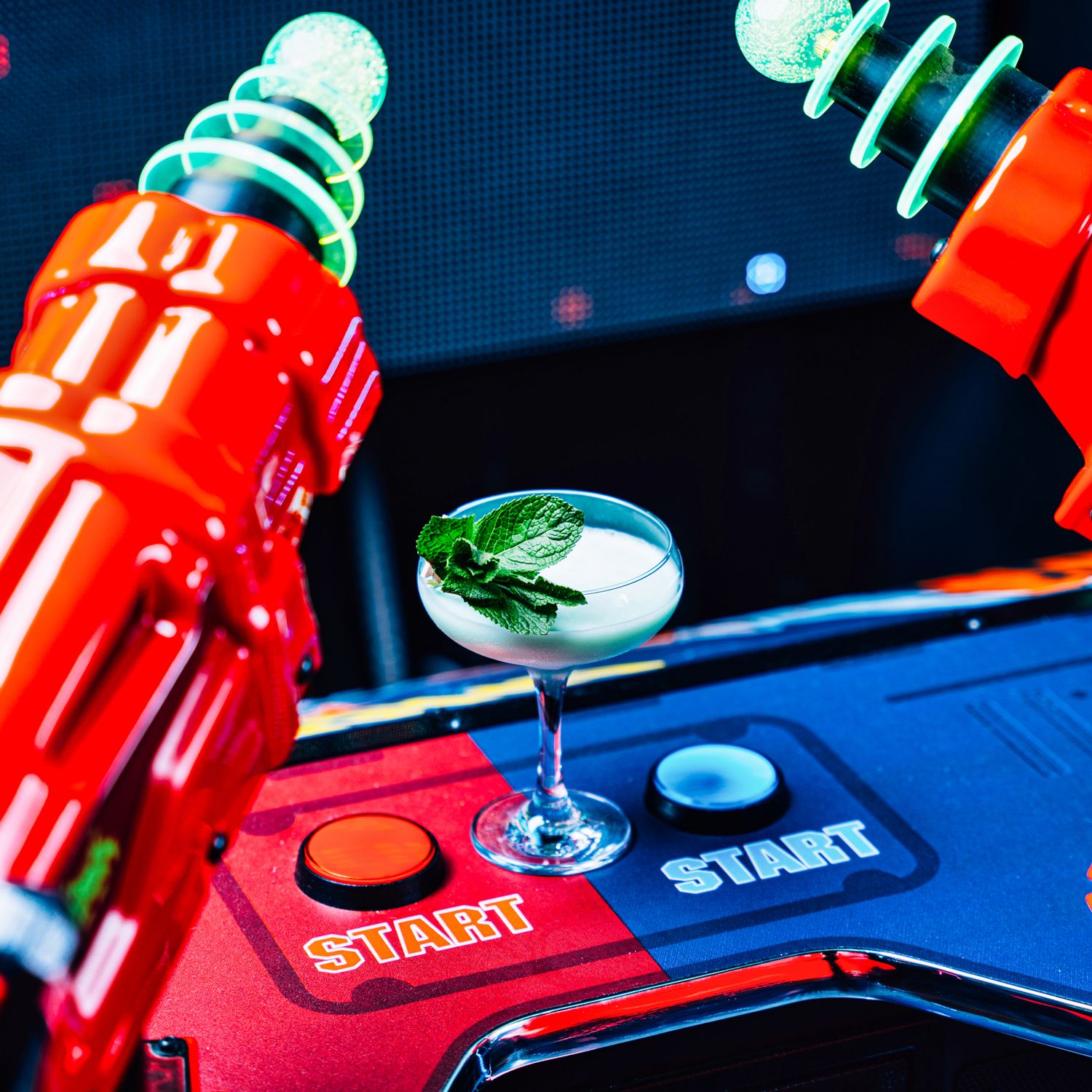 Green herb garnished cocktail in coupe glass held by red arcade robot claw machine.