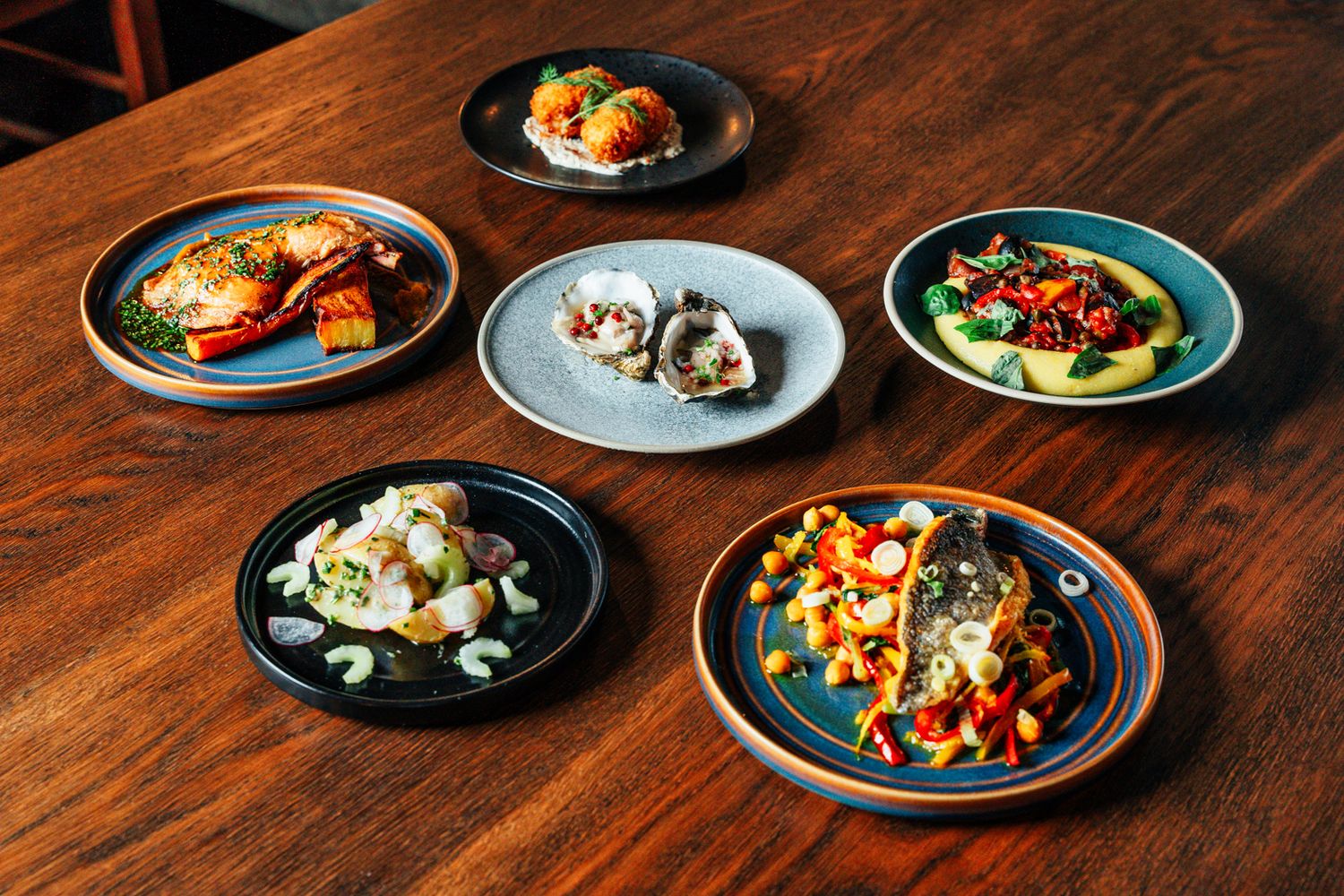 Six colorful seafood and vegetable dishes arranged on various ceramic plates on a rustic wooden table.