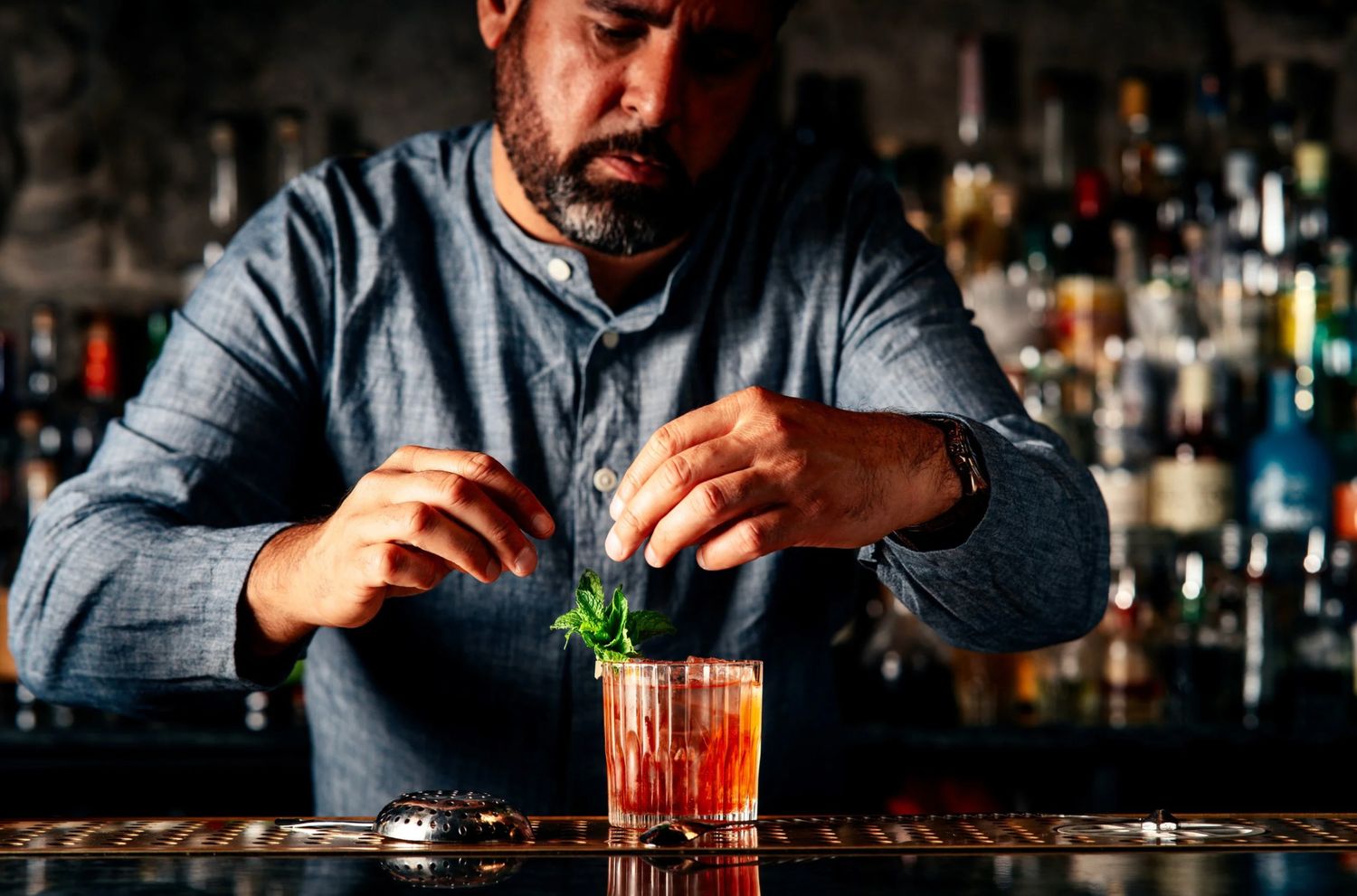 Bartender carefully garnishing a red cocktail with fresh mint at an upscale bar.