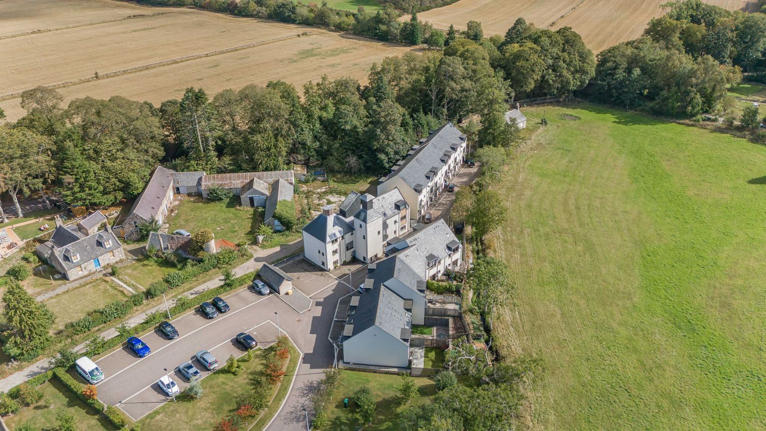 Aerial view of a residential apartment complex surrounded by lush green countryside and parking area.
