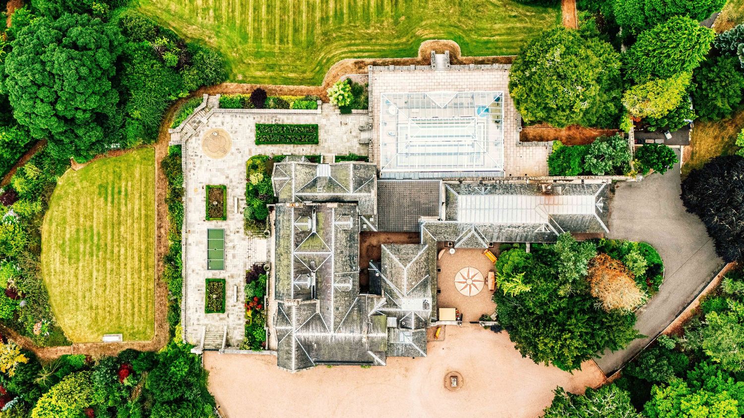 Aerial view of a grand country estate surrounded by lush green gardens, manicured lawns, and mature trees.