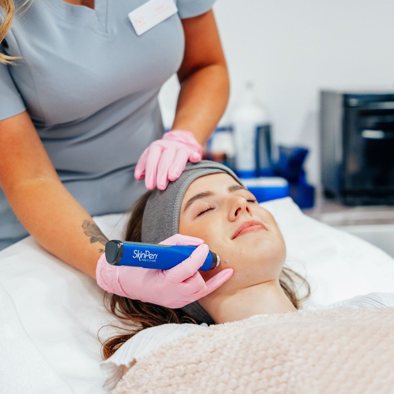 Skincare professional using a SkinPen microneedling device on a female client's face in a treatment room.