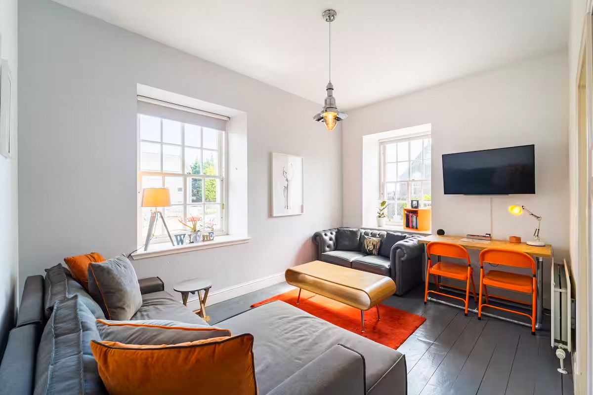 Contemporary living room with grey sofas, orange rug, wall-mounted TV, and wooden flooring.