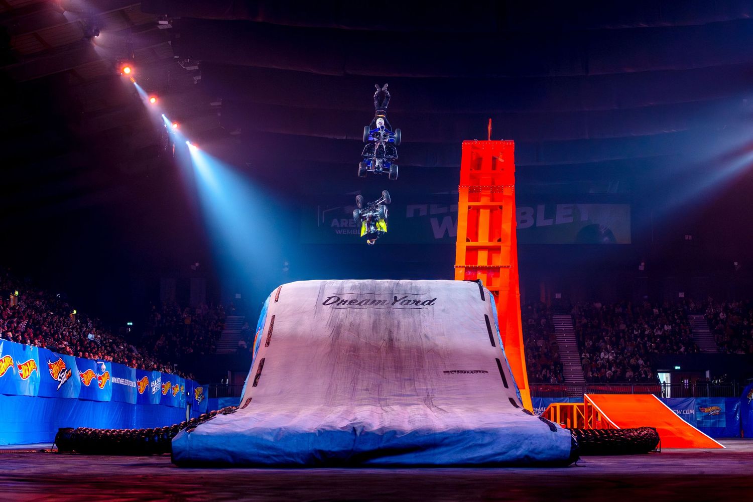 Stunt rider performs a high-flying aerial trick over a Dream Yard ramp in a packed indoor arena.