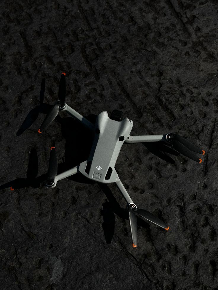 DJI Mini drone with propellers extended resting on dark textured ground surface.