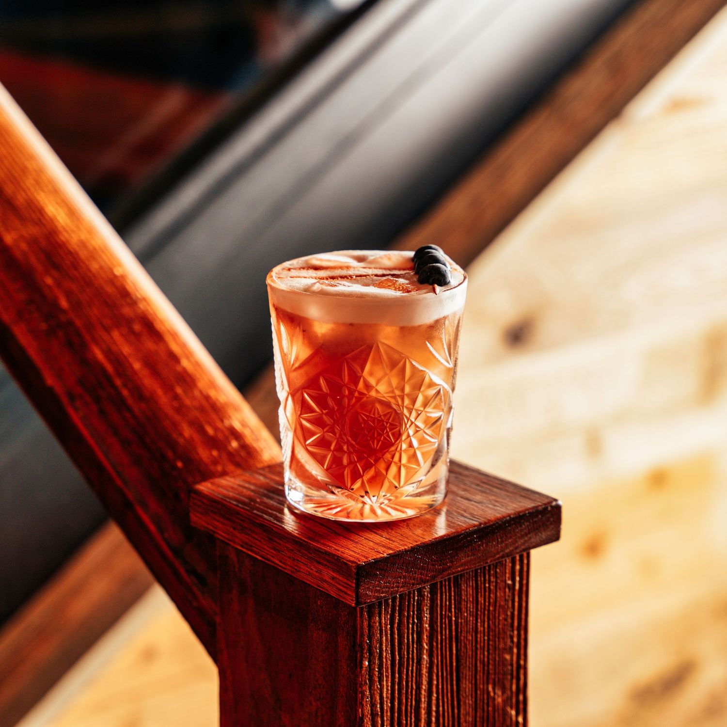 Crystal cut rocks glass with a pink cocktail garnished with berries resting on a wooden railing.