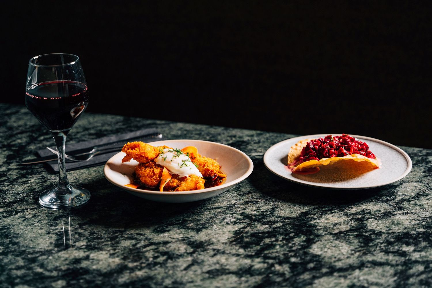 Two plates of Italian food and a glass of red wine on a dark marble table in a restaurant.