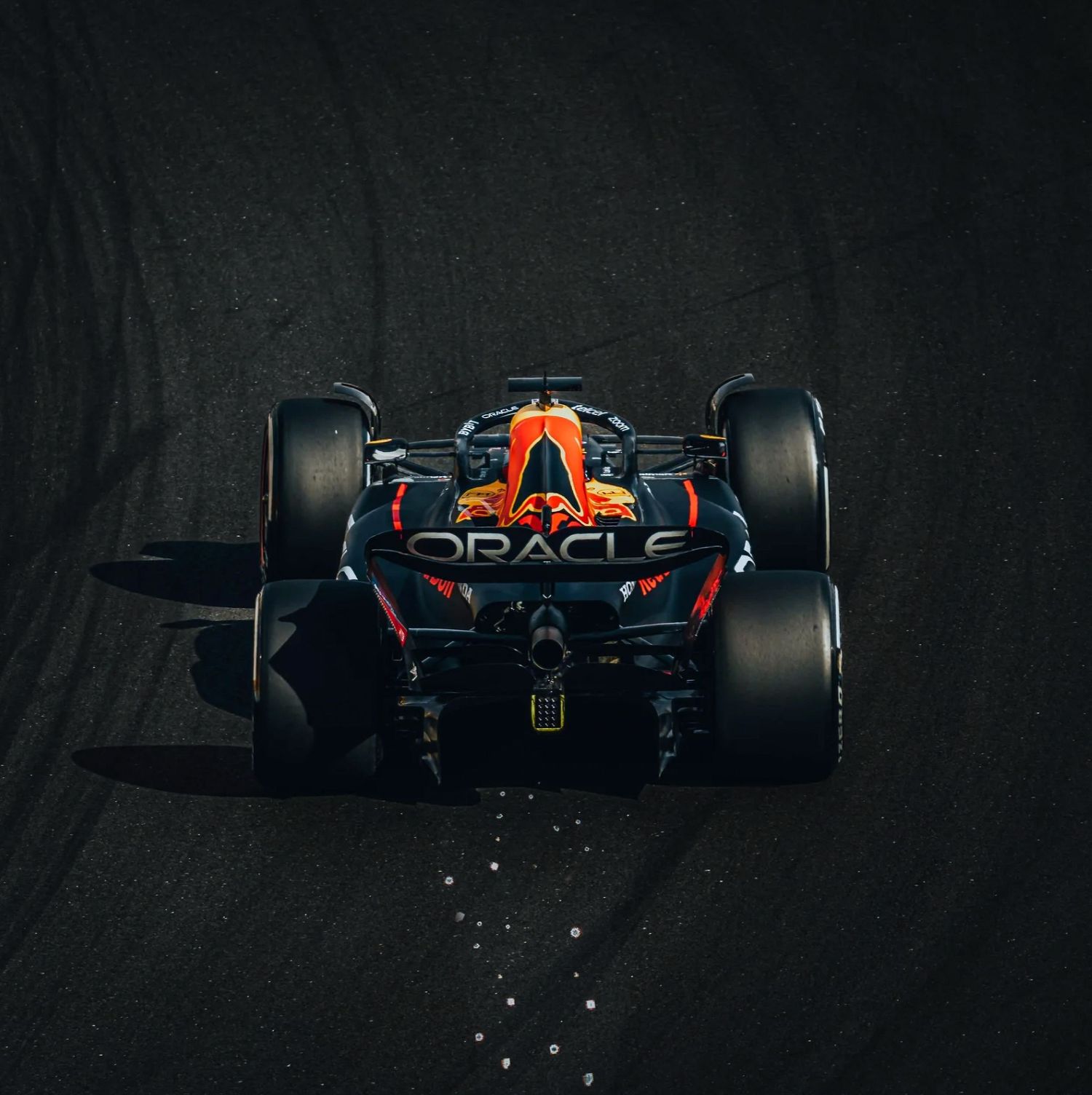 Aerial view of Oracle Red Bull Racing F1 car on dark track, showcasing red and orange livery with large rear tires.