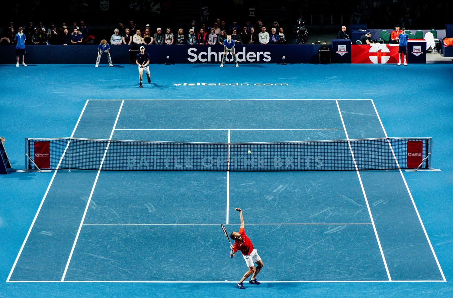 Aerial view of Battle of the Brits tennis match on blue court with Schroders branding.