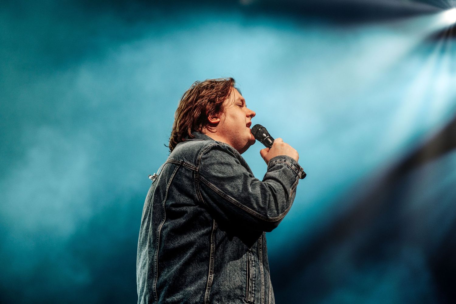 Singer performing on stage with microphone under blue smoky concert lighting.