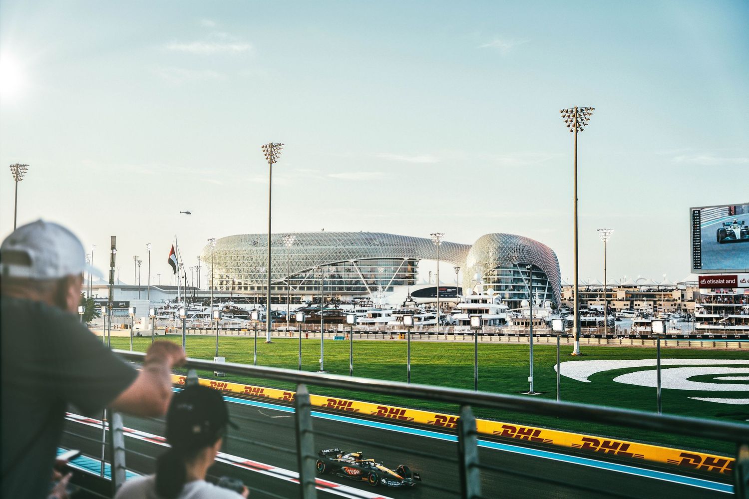 Formula 1 car racing past spectators at Yas Marina Circuit with Yas Hotel in background.