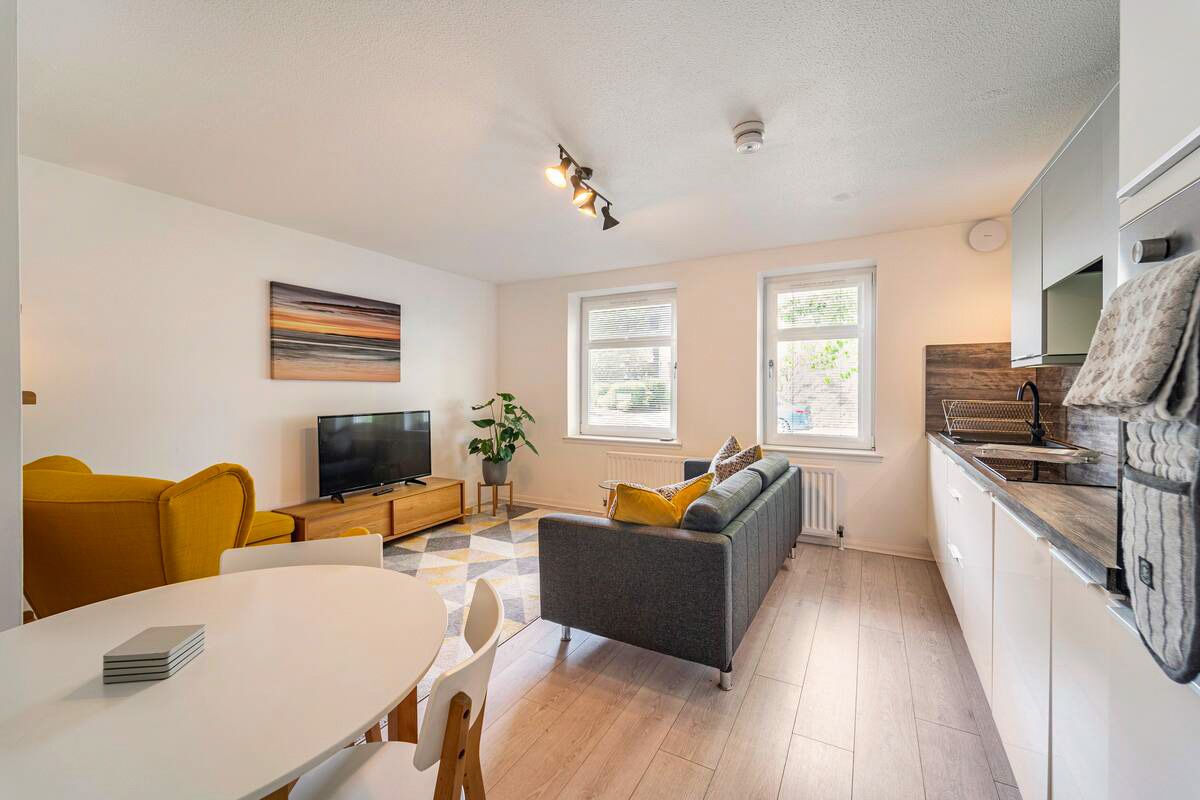 Bright contemporary living space with yellow armchairs, grey sofa, white dining table, and wood floors.