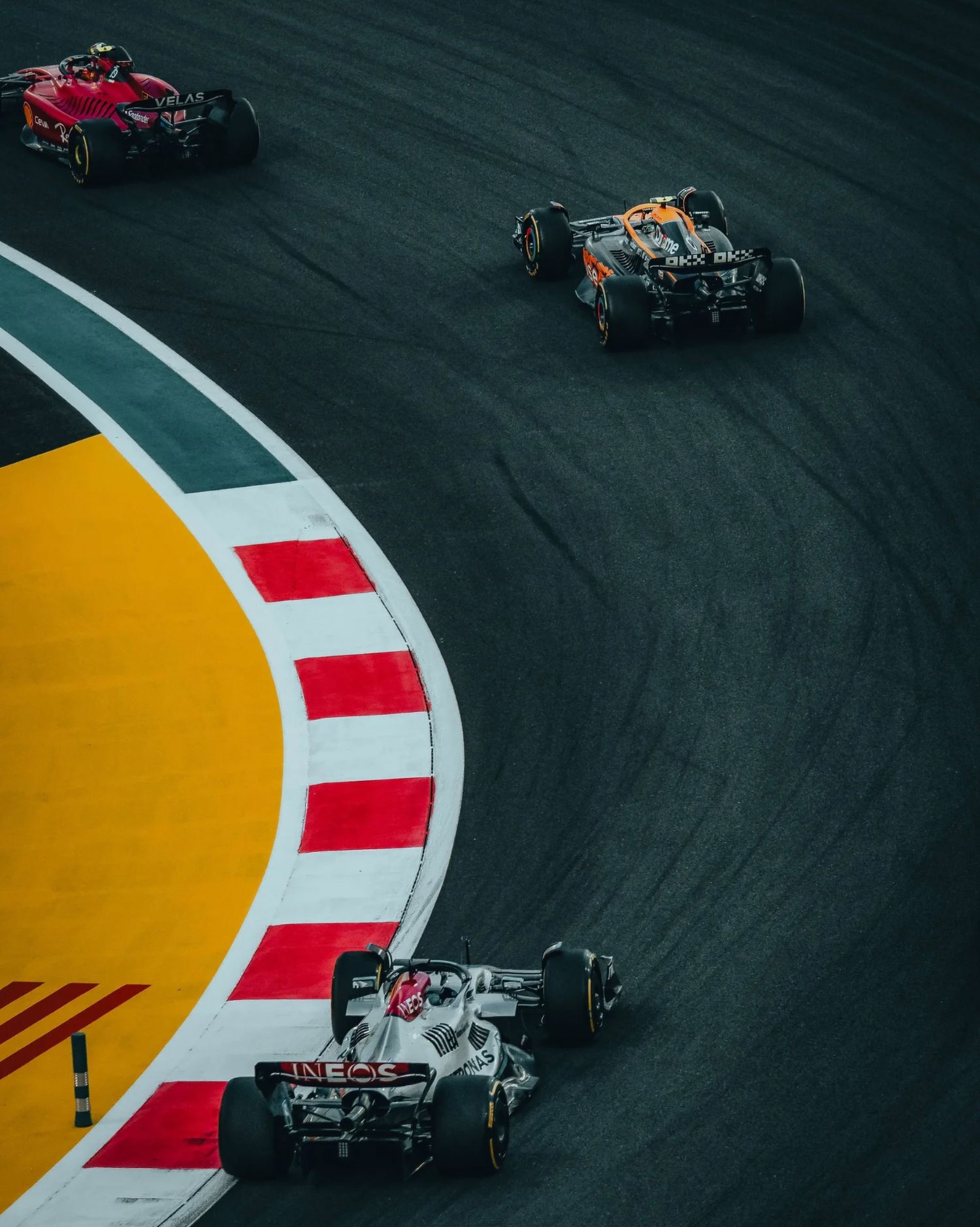 Three Formula 1 race cars navigate a colorful curb on a winding circuit during a Grand Prix race.