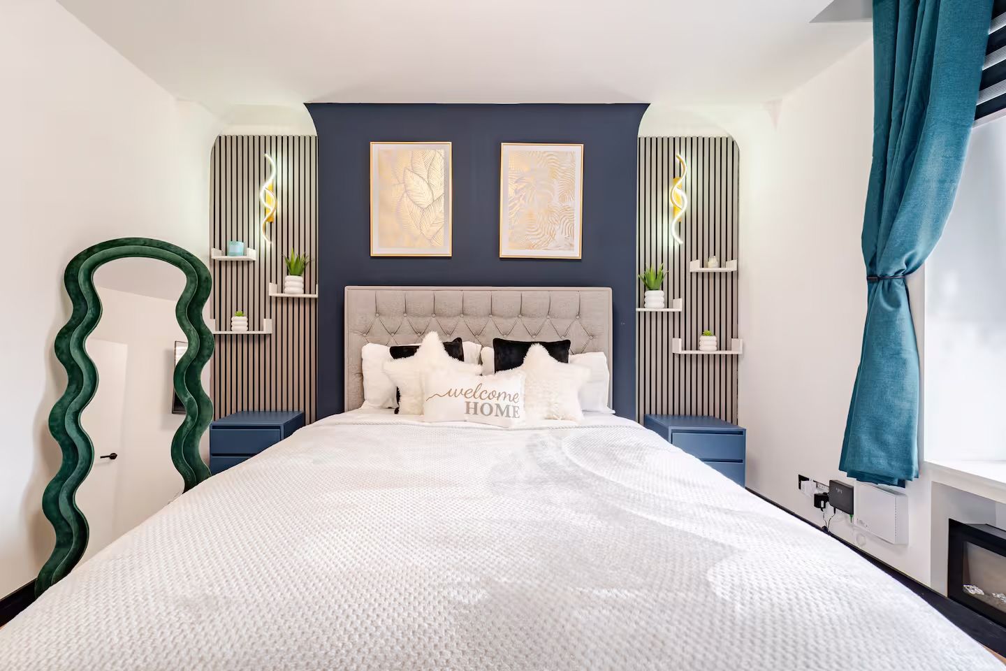 Stylish bedroom featuring blue accent wall, tufted headboard, white bedding, decorative shelving, and teal curtains.