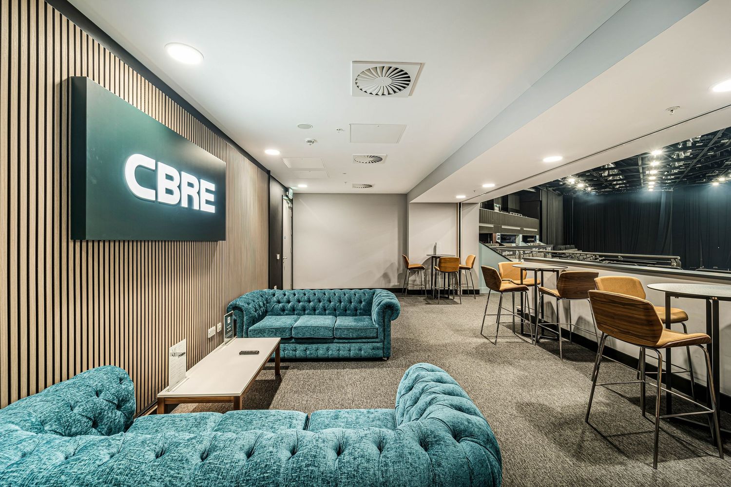 Spacious CBRE office reception lounge featuring teal velvet sofas, wood slat walls, and a bar area.