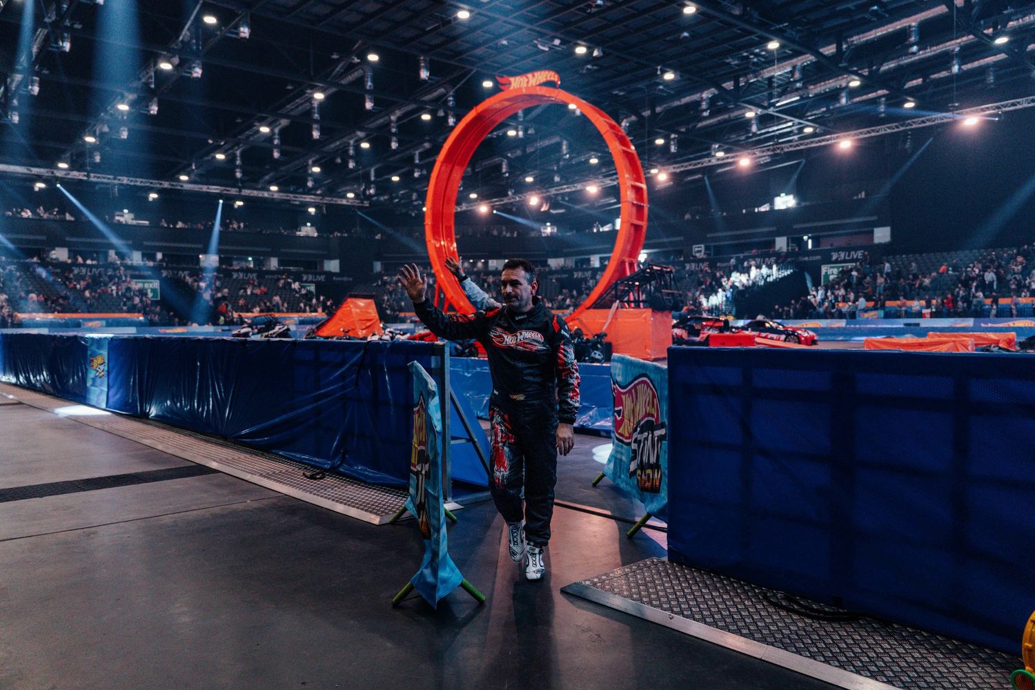 A performer stands before a giant red loop at an indoor Hot Wheels Stunt Show event.