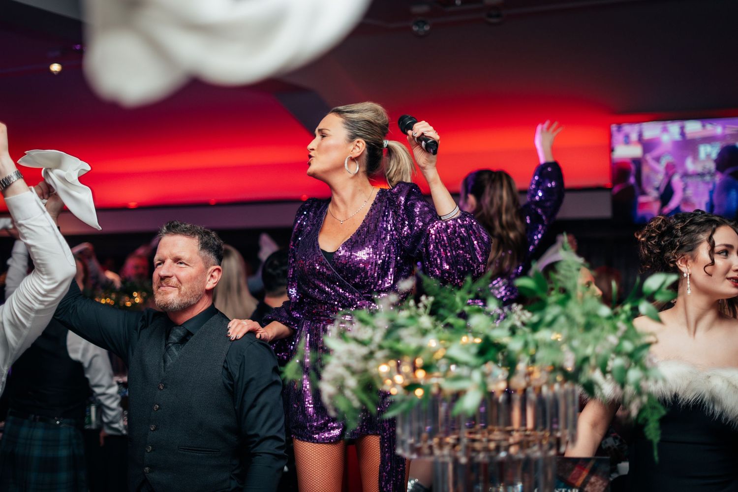 A woman in a purple sequin dress sings with a microphone at a festive Burns Night gala dinner.