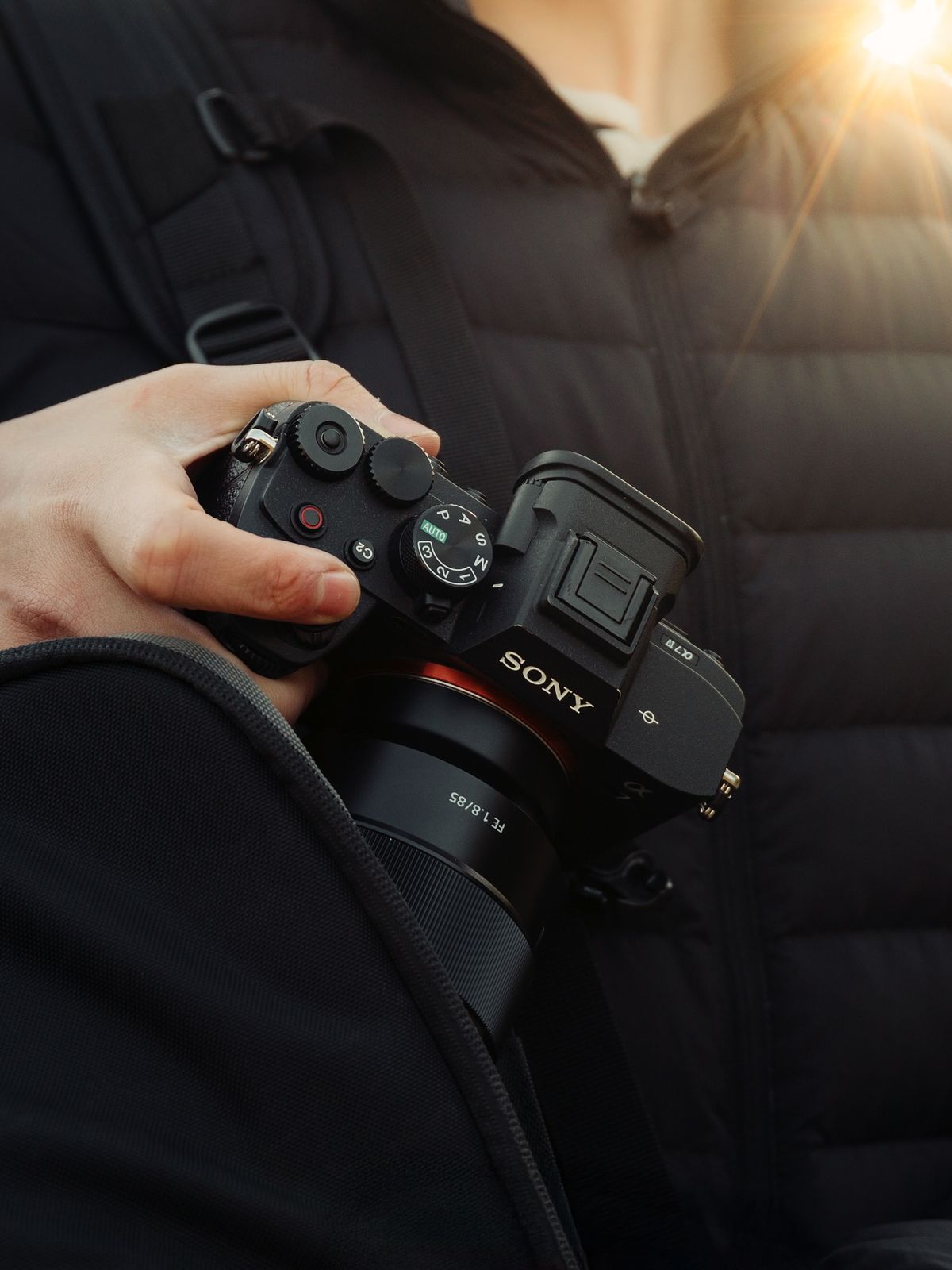 Person holding Sony mirrorless camera with lens outdoors with golden sunlight in background.