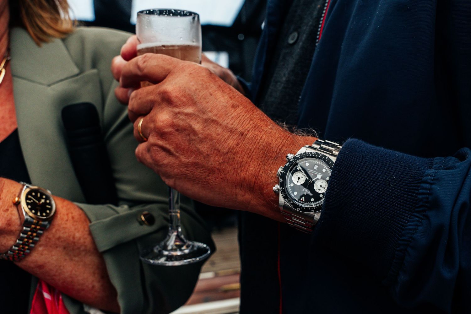 Close-up of hands holding champagne glasses, one wearing a silver chronograph watch.