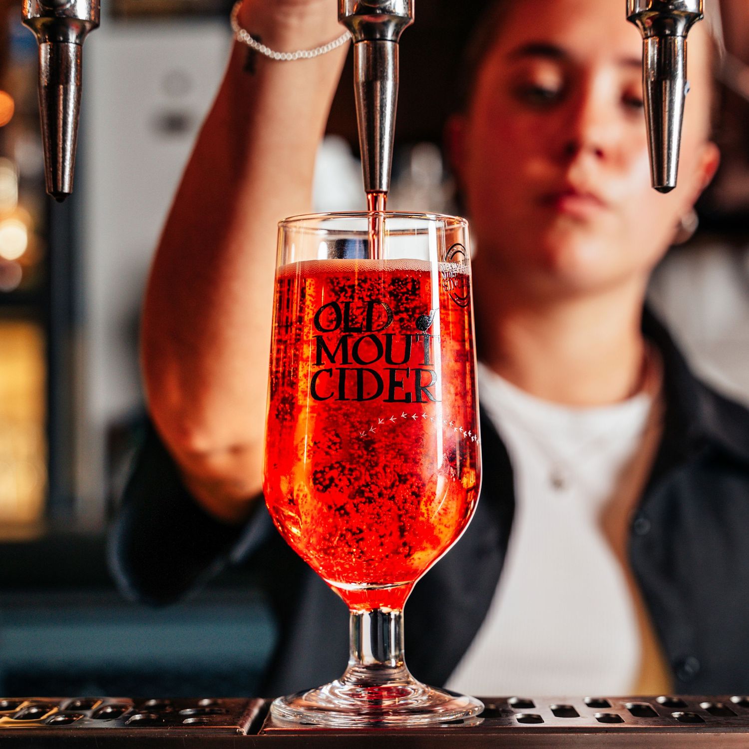 Bartender pouring vibrant red Old Mout Cider into a branded glass from a draught tap.