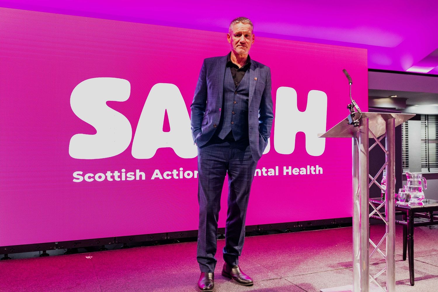Man standing confidently in front of SAMH Scottish Action Mental Health pink backdrop.