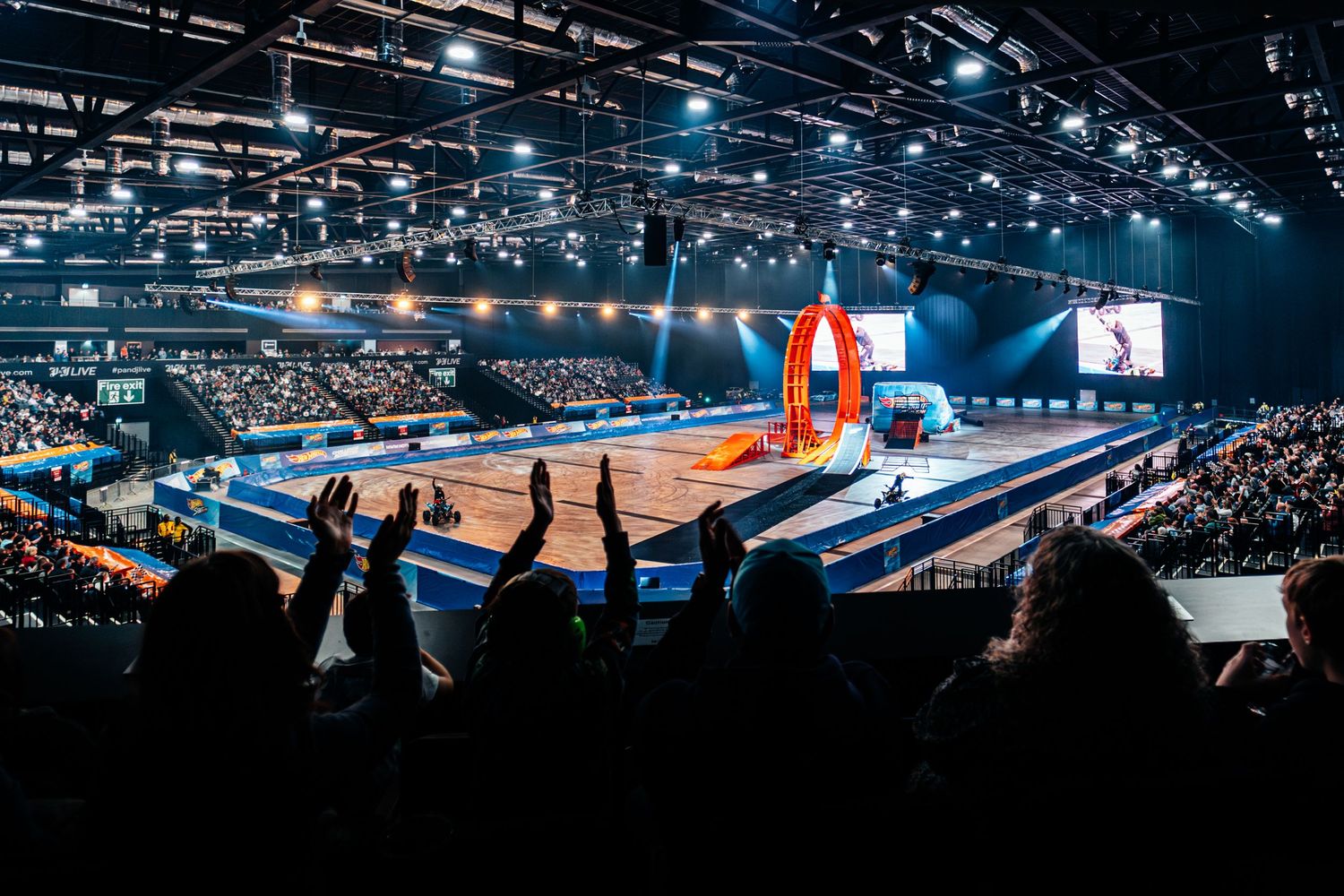 Excited crowd watching a Hot Wheels stunt show with loop track inside a large arena.