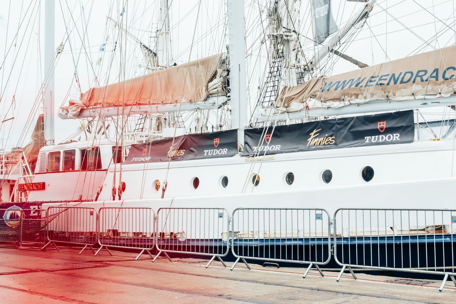 Historic tall ship Pendragon docked at port with white hull, portholes, and rigging visible behind metal barriers.