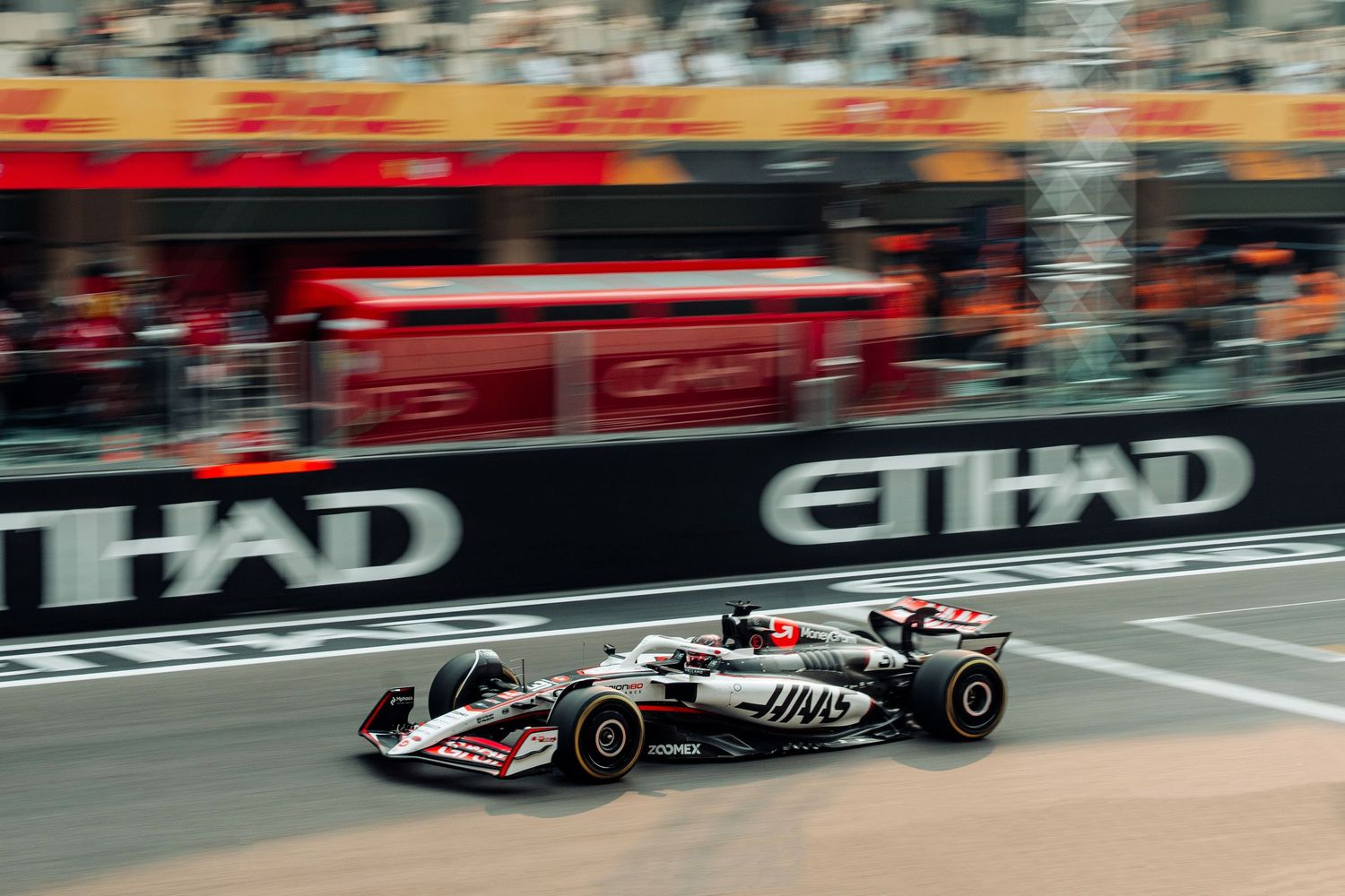 Haas F1 car racing past Etihad advertising boards on a blurred circuit track.