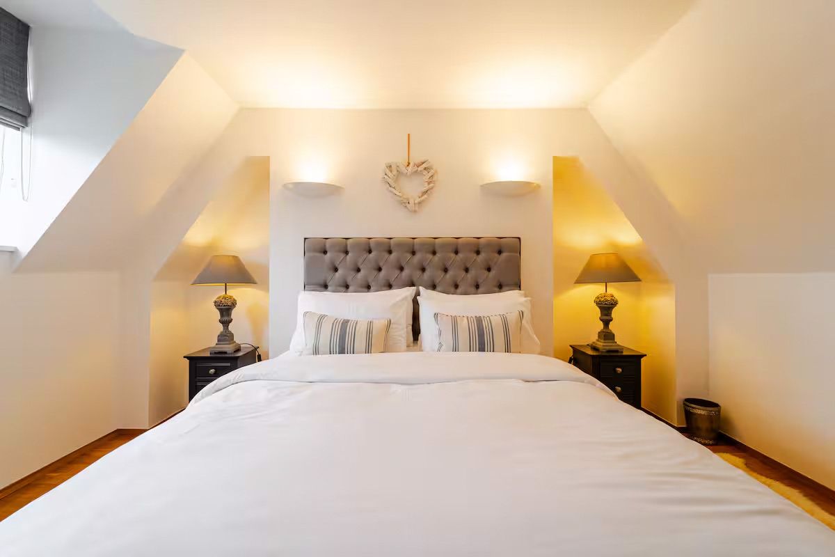 Luxurious double bedroom with tufted grey headboard, crisp white bedding, and warm bedside lamps.