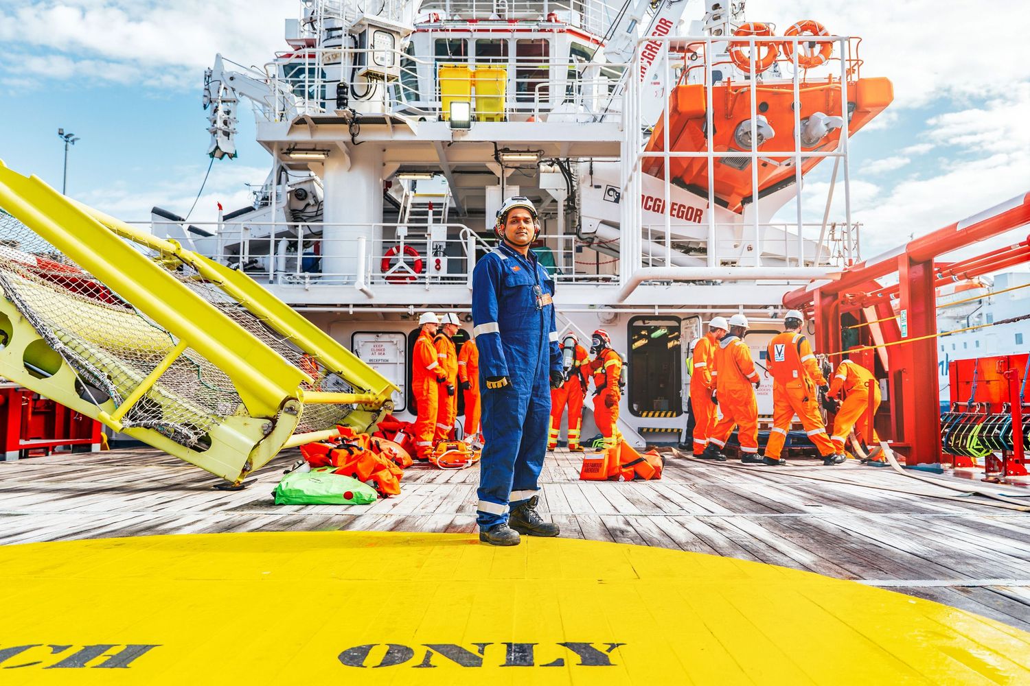 Offshore crew members in orange safety suits gather on the deck of a large industrial vessel during operations.